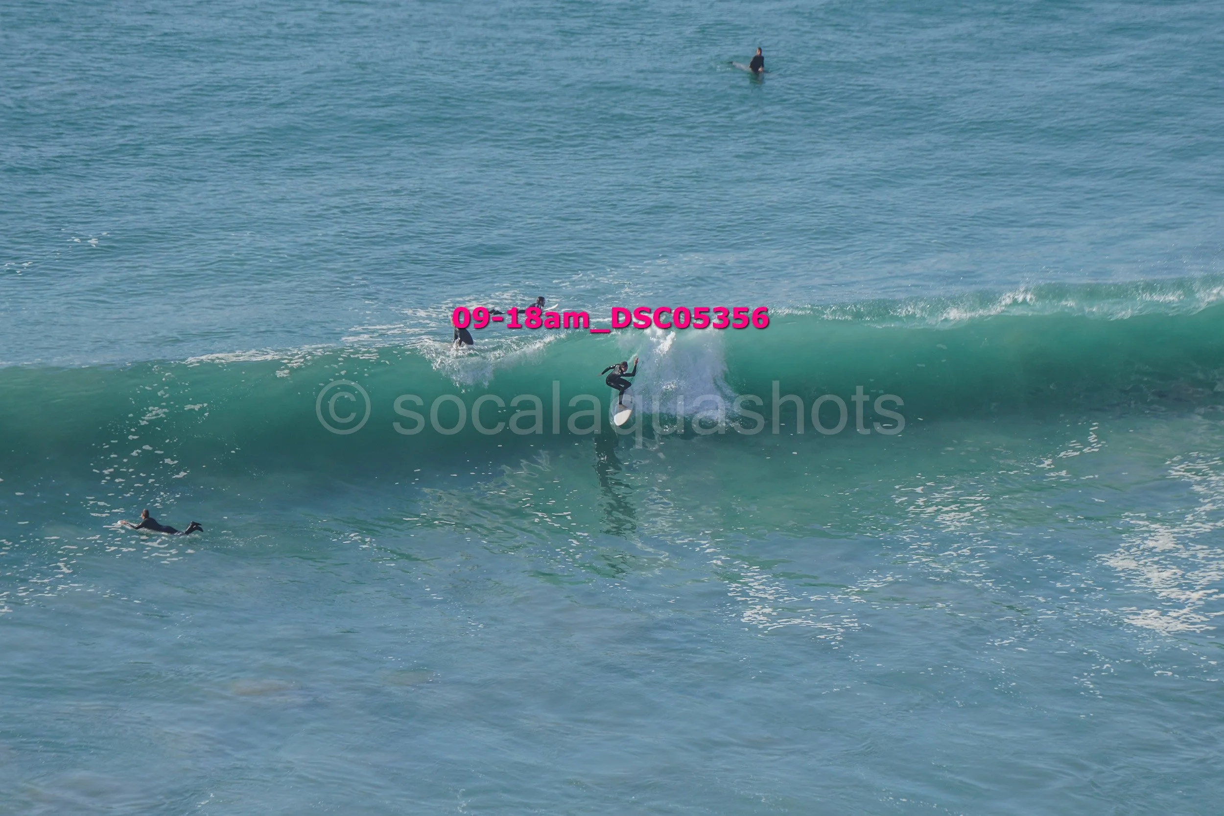 Surfer riding a wave with others in the water and a surfer paddleboarding in the background.