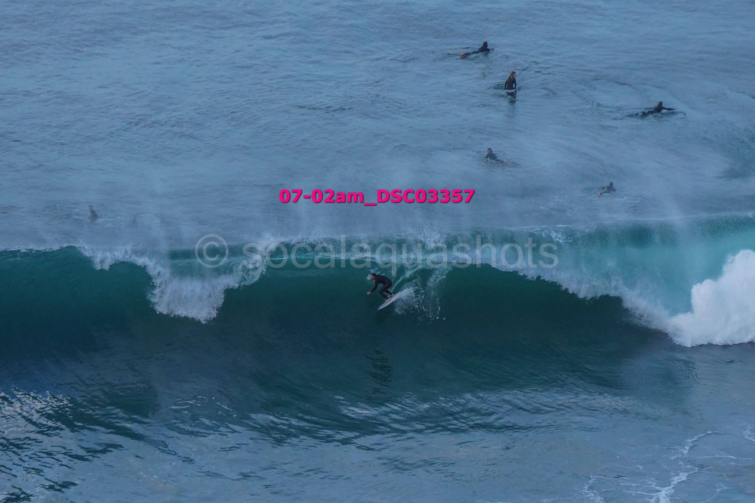 Surfer riding a wave while multiple surfers and paddleboarders are in the water