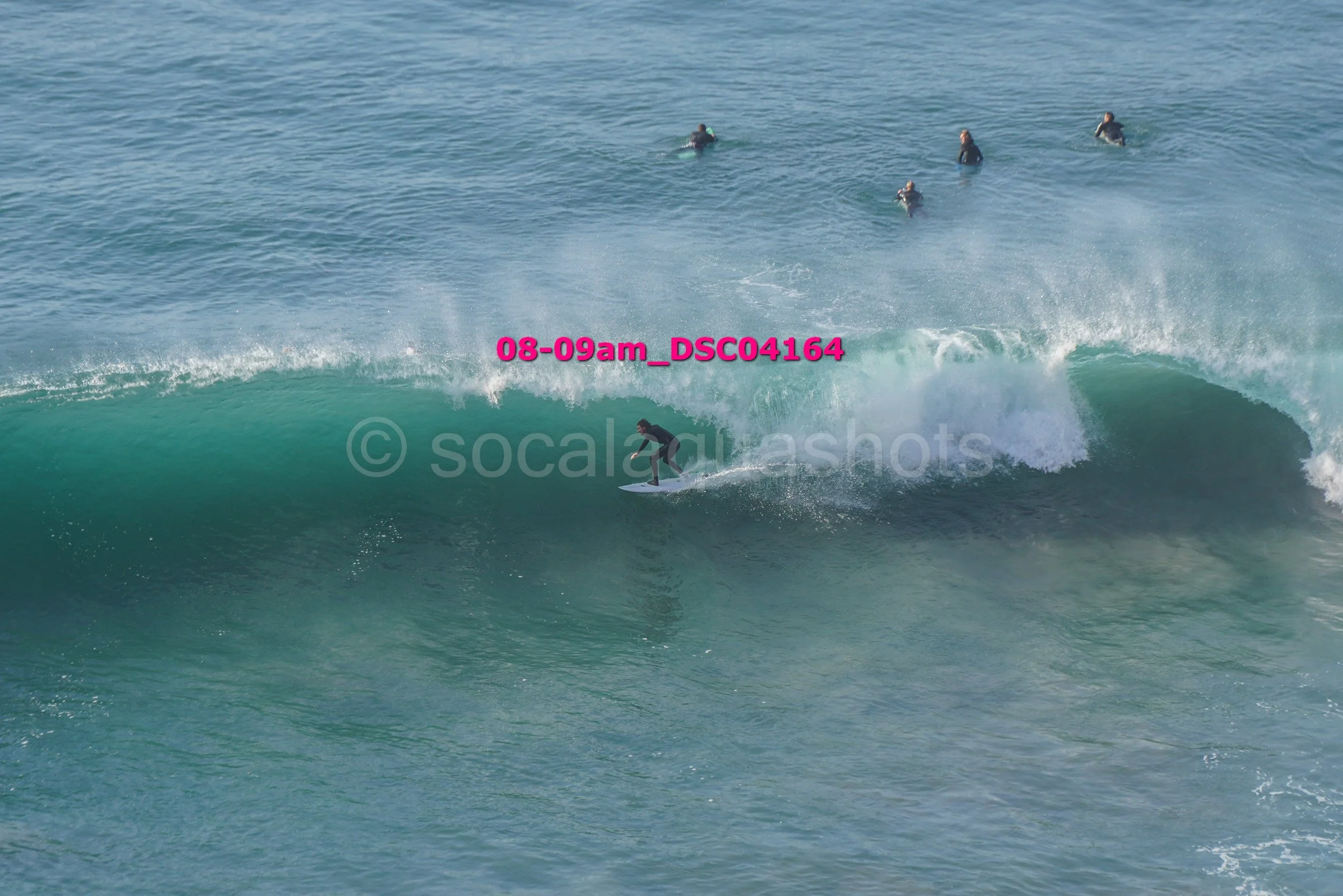 Surfer riding a wave with several people swimming in the water in the background.
