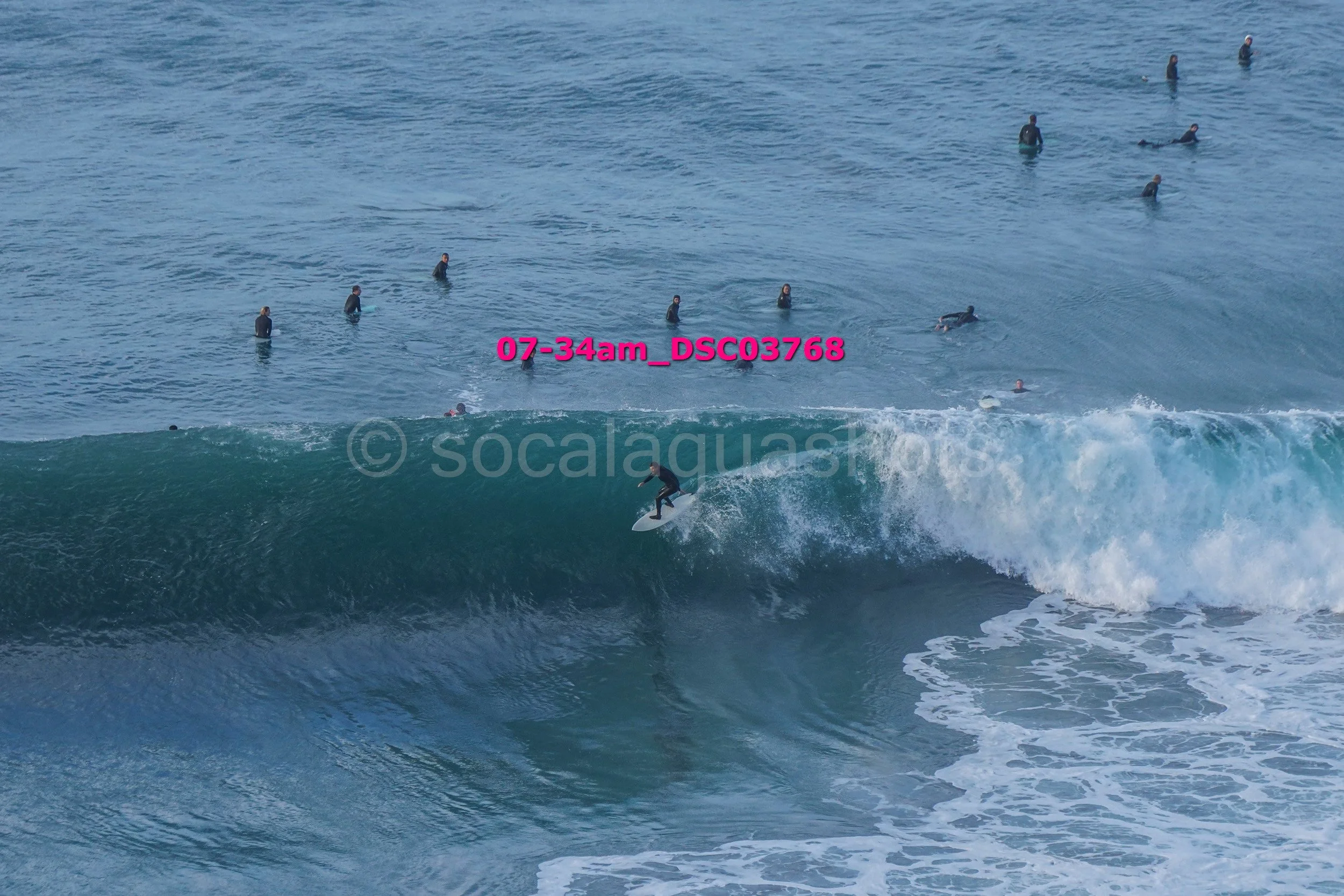 A person surfing on a large wave with several people in the water in the background.