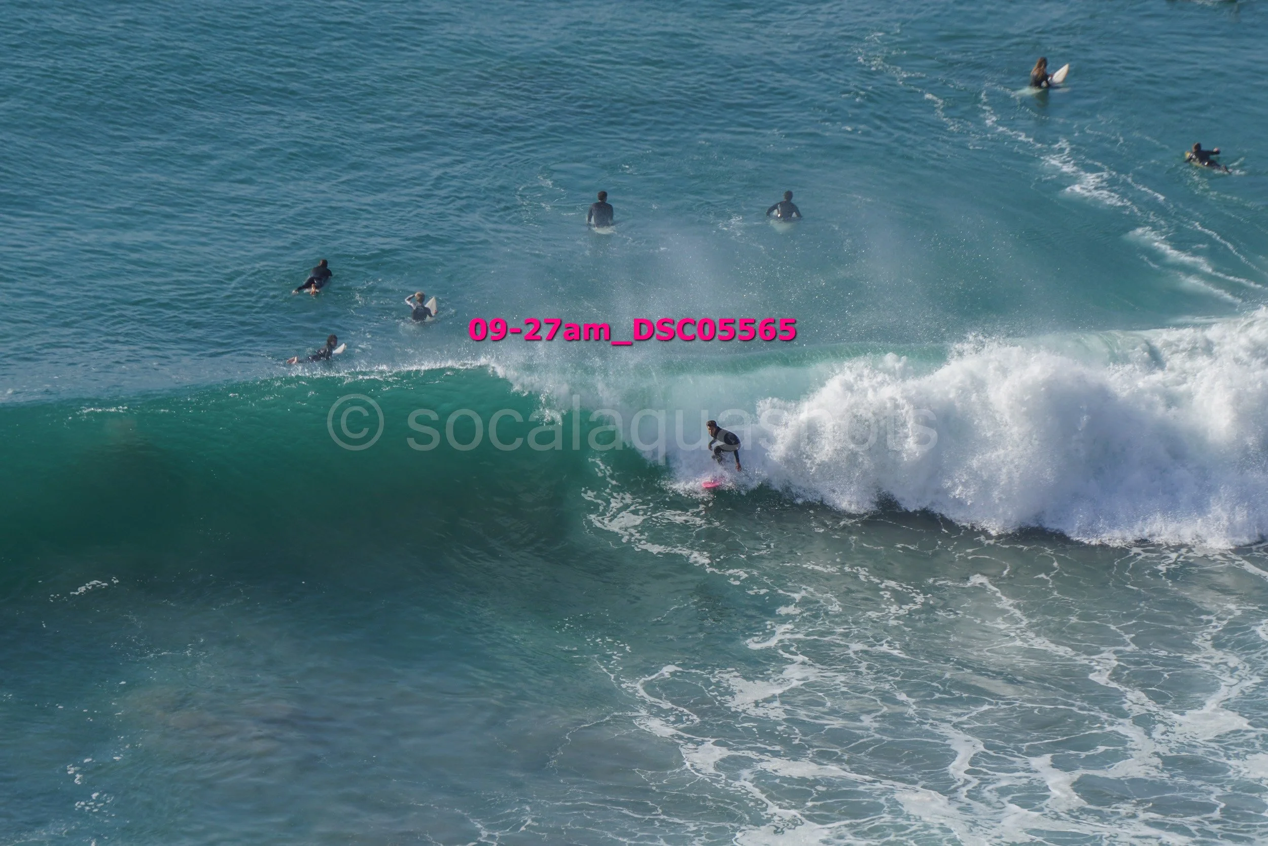 Surfer riding a large wave with several people in the water watching from behind.