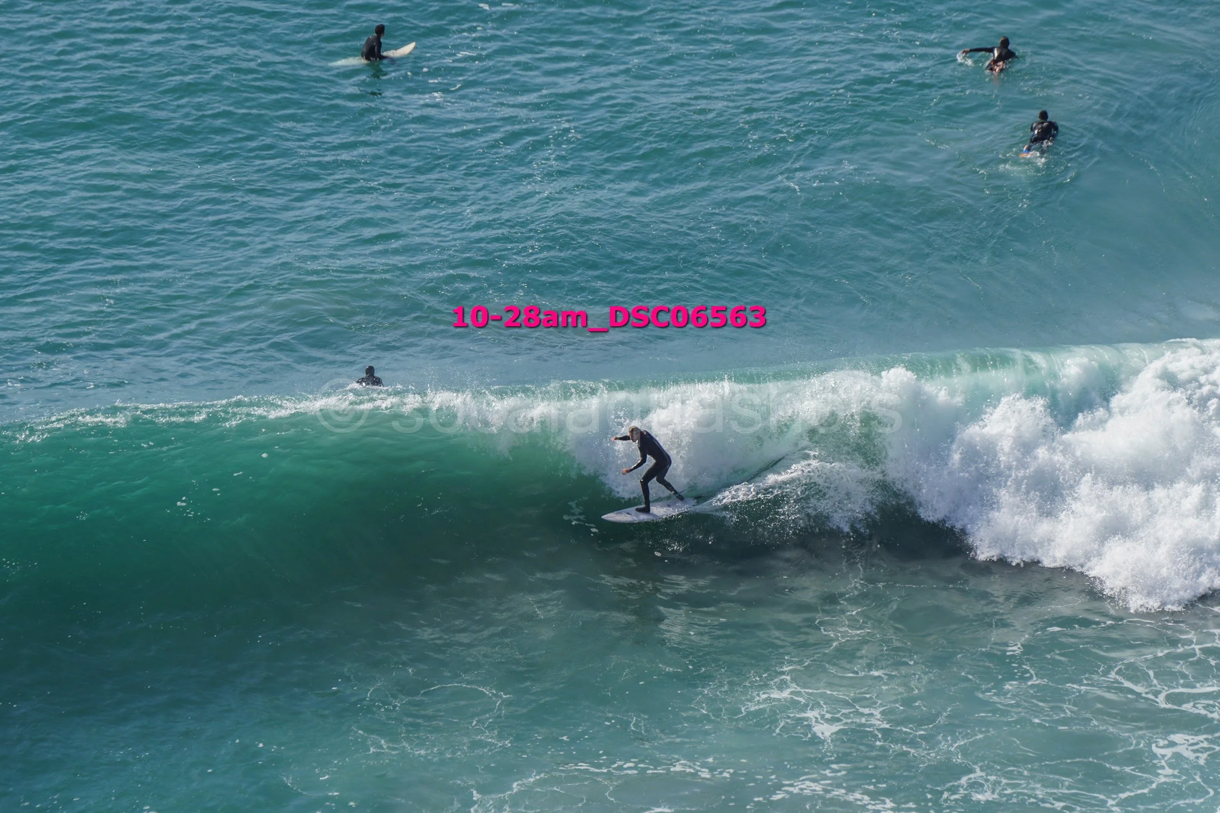 Surfer riding a wave in the ocean with several people paddleboarding in the background.