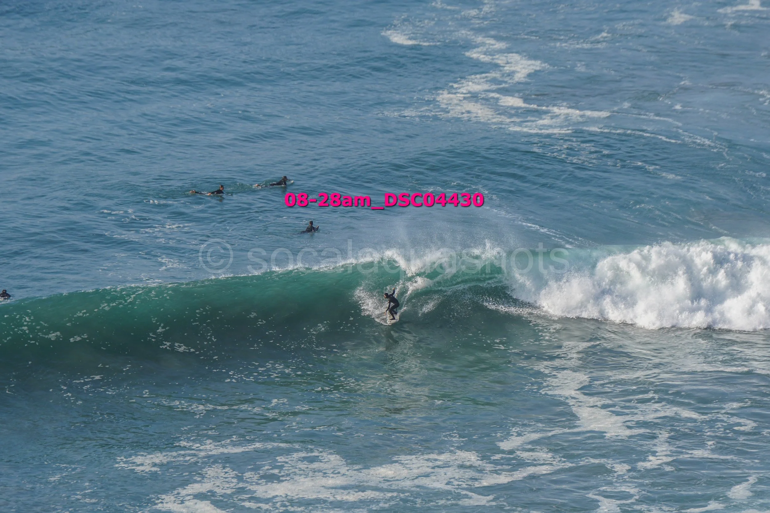 A person surfing on a wave with several other surfers in the water nearby