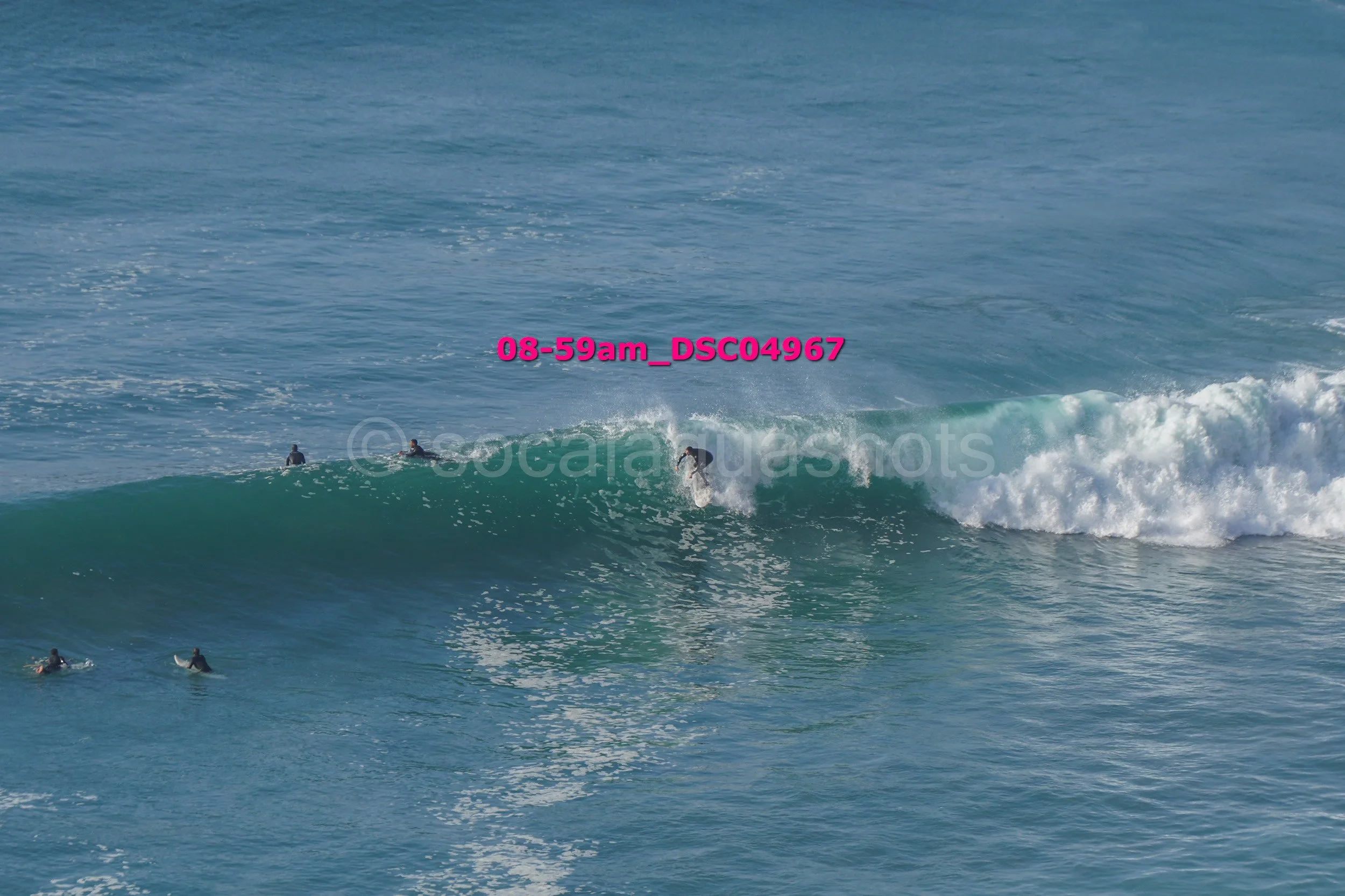 A surfer riding a wave in the ocean, with several other surfers in the water nearby.