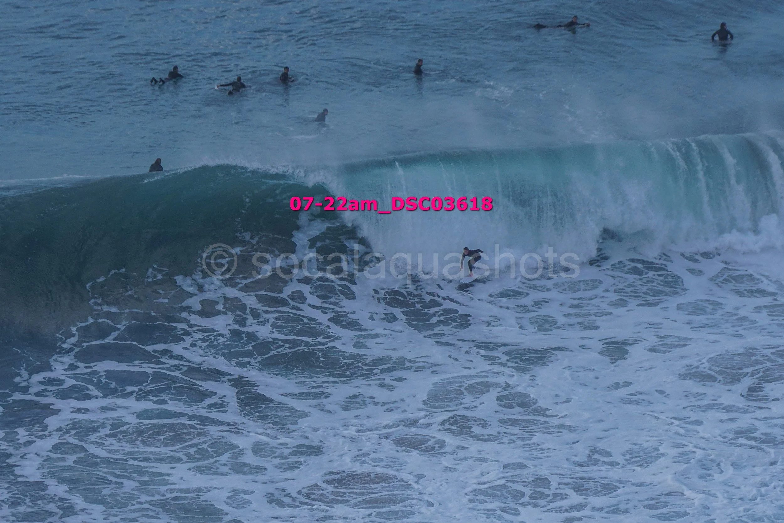 A group of people in wetsuits surfing and swimming in the ocean with one surfer riding a wave.