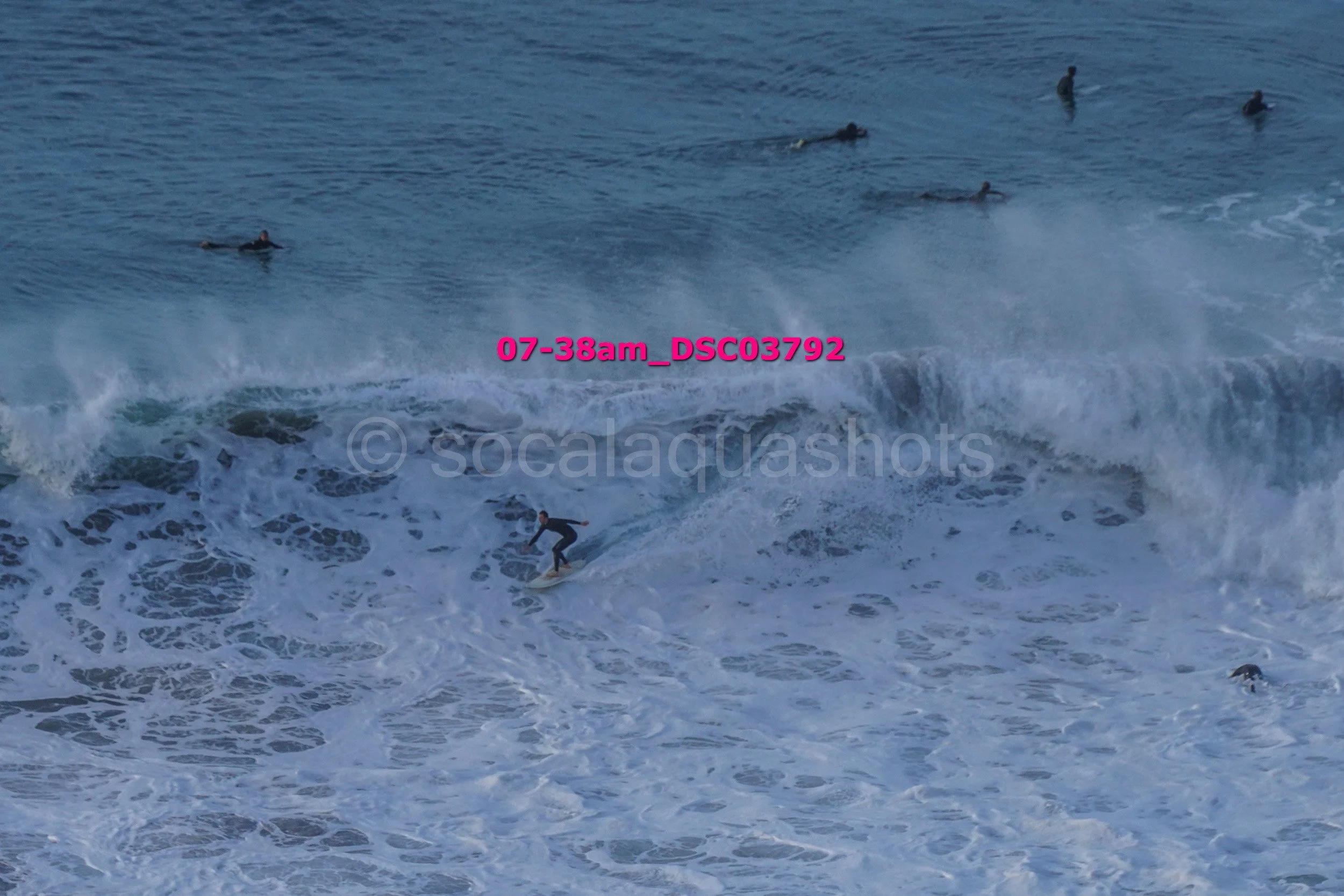Surfers in the ocean riding and swimming through large, white-capped waves.