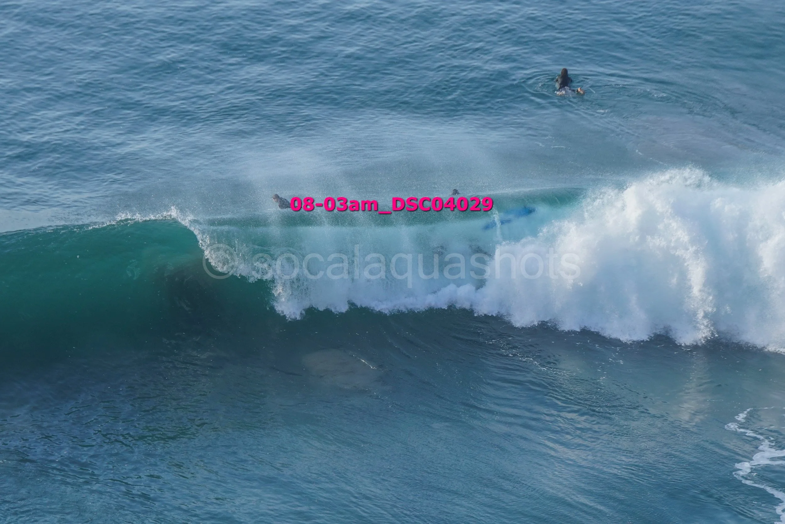 Surfer in the water riding a wave while another swimmer floats in the background.