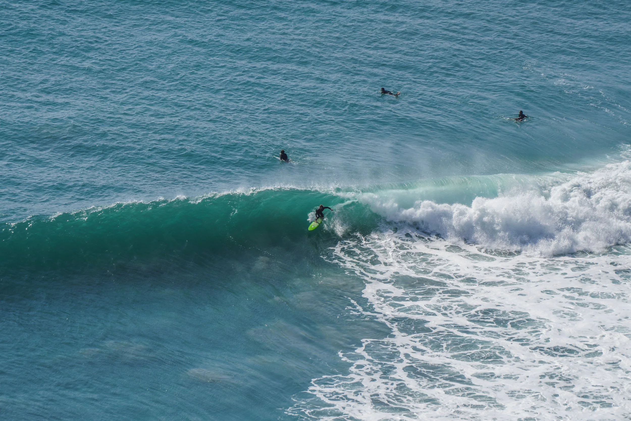 Surfer riding a wave while four other surfers are in the water in the background.