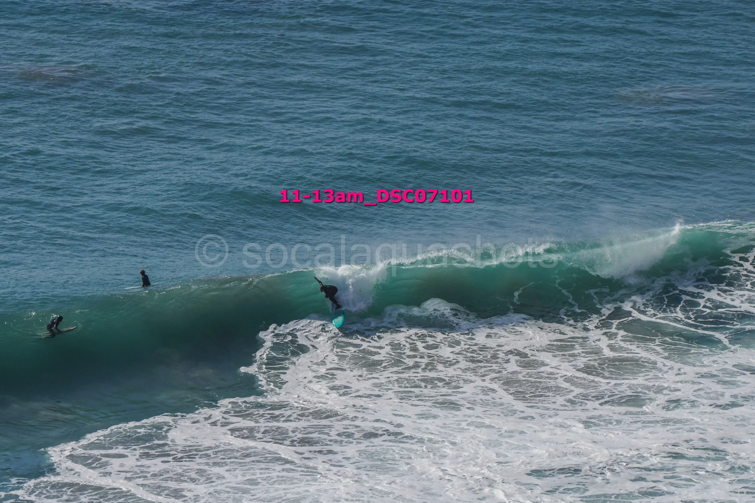A person surfing on a large wave with three other surfers in the water nearby.