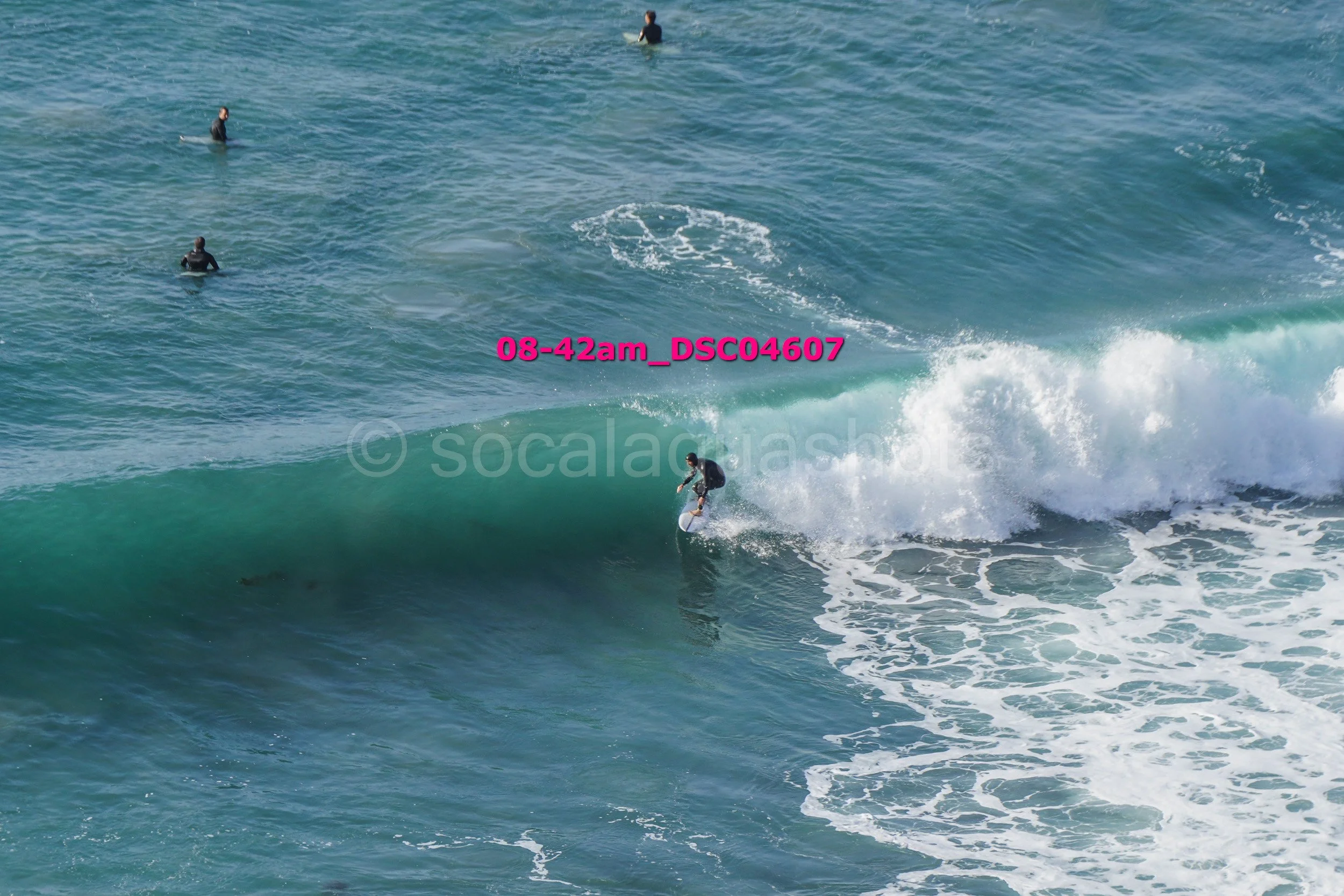 A person surfing on a wave in the ocean with three other surfers in the background.