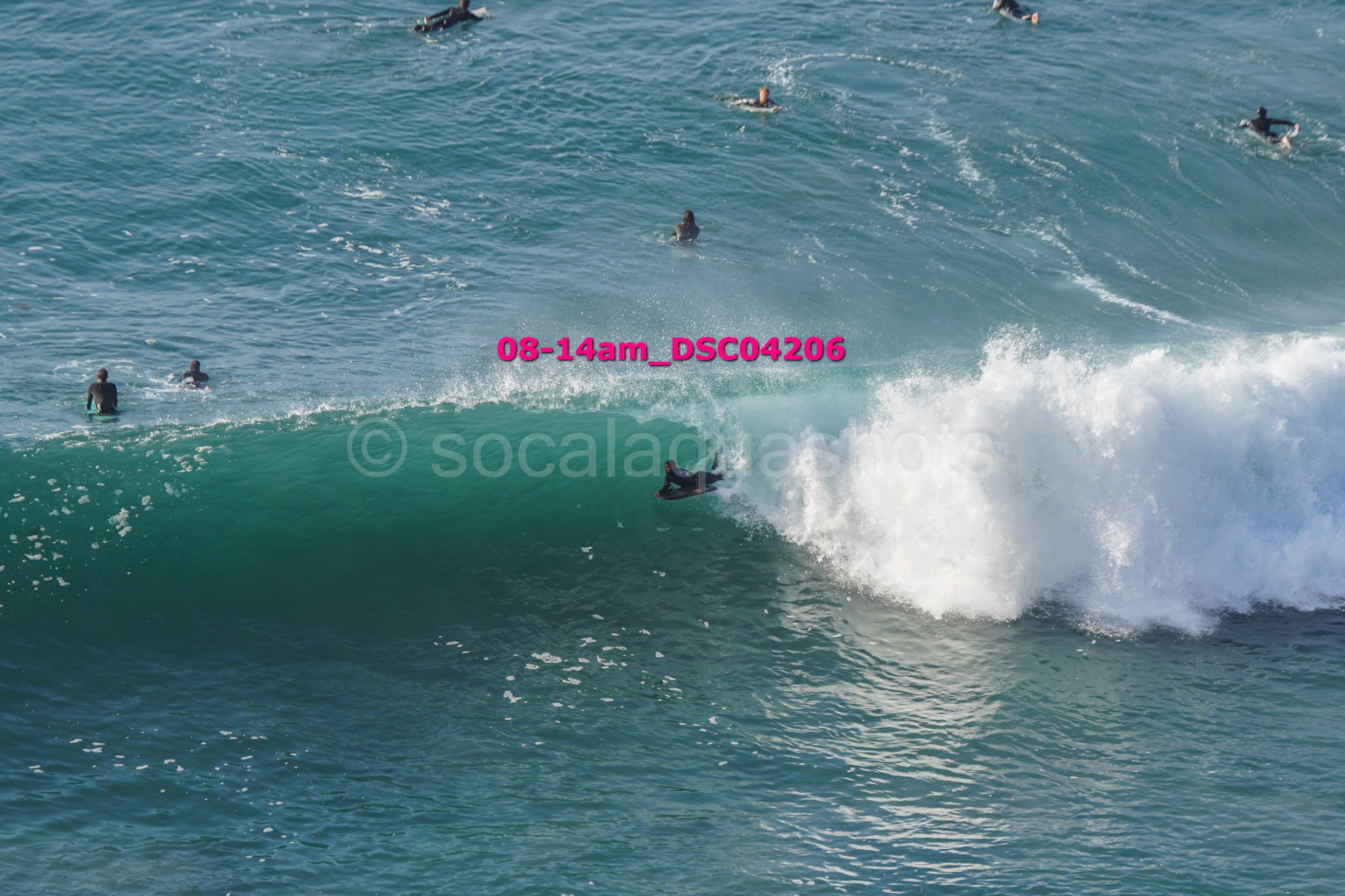 A group of people surfing in the ocean, with one person riding a large waves while others are paddling or swimming nearby.