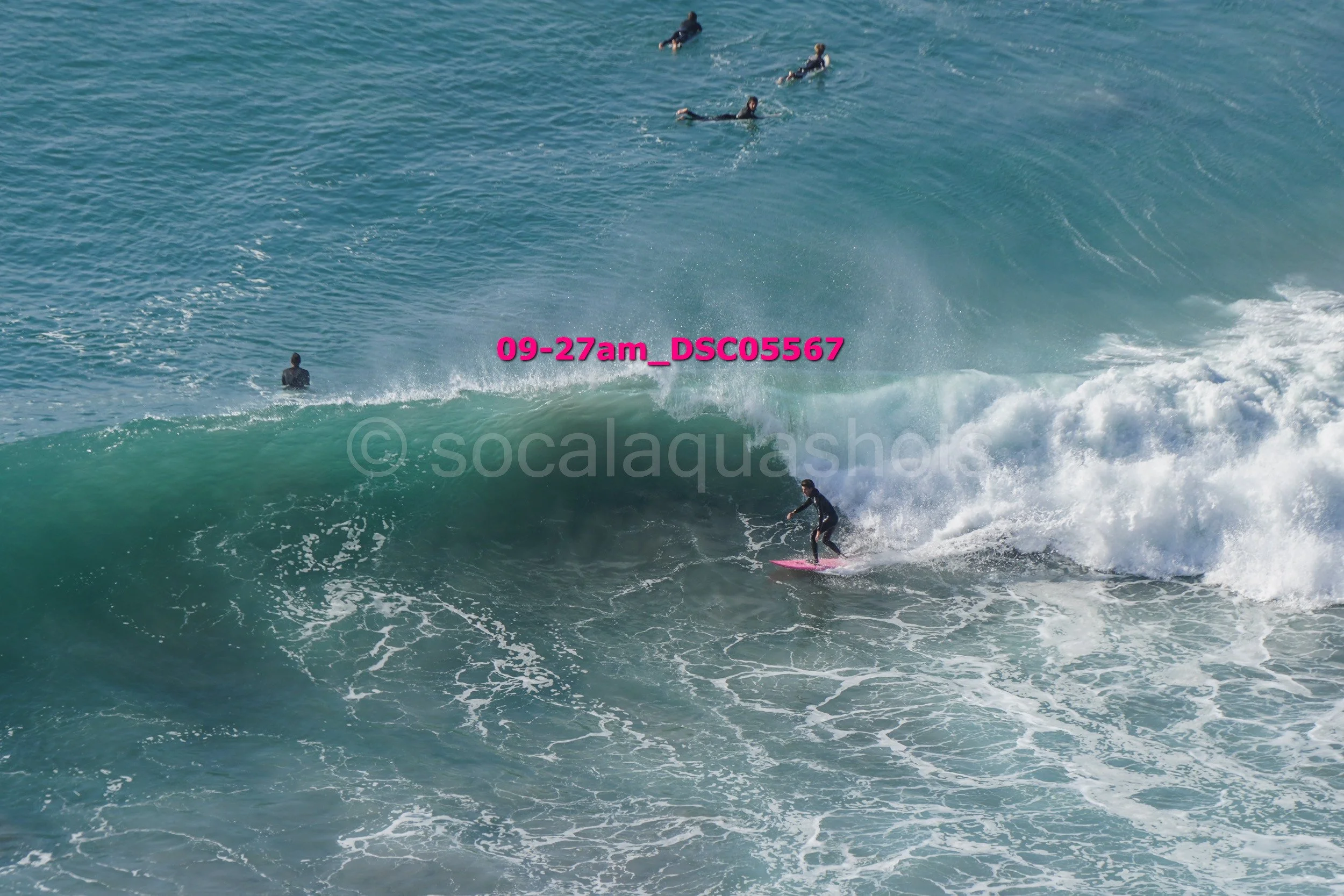 Surfer riding a wave with other surfers floating in the water nearby.