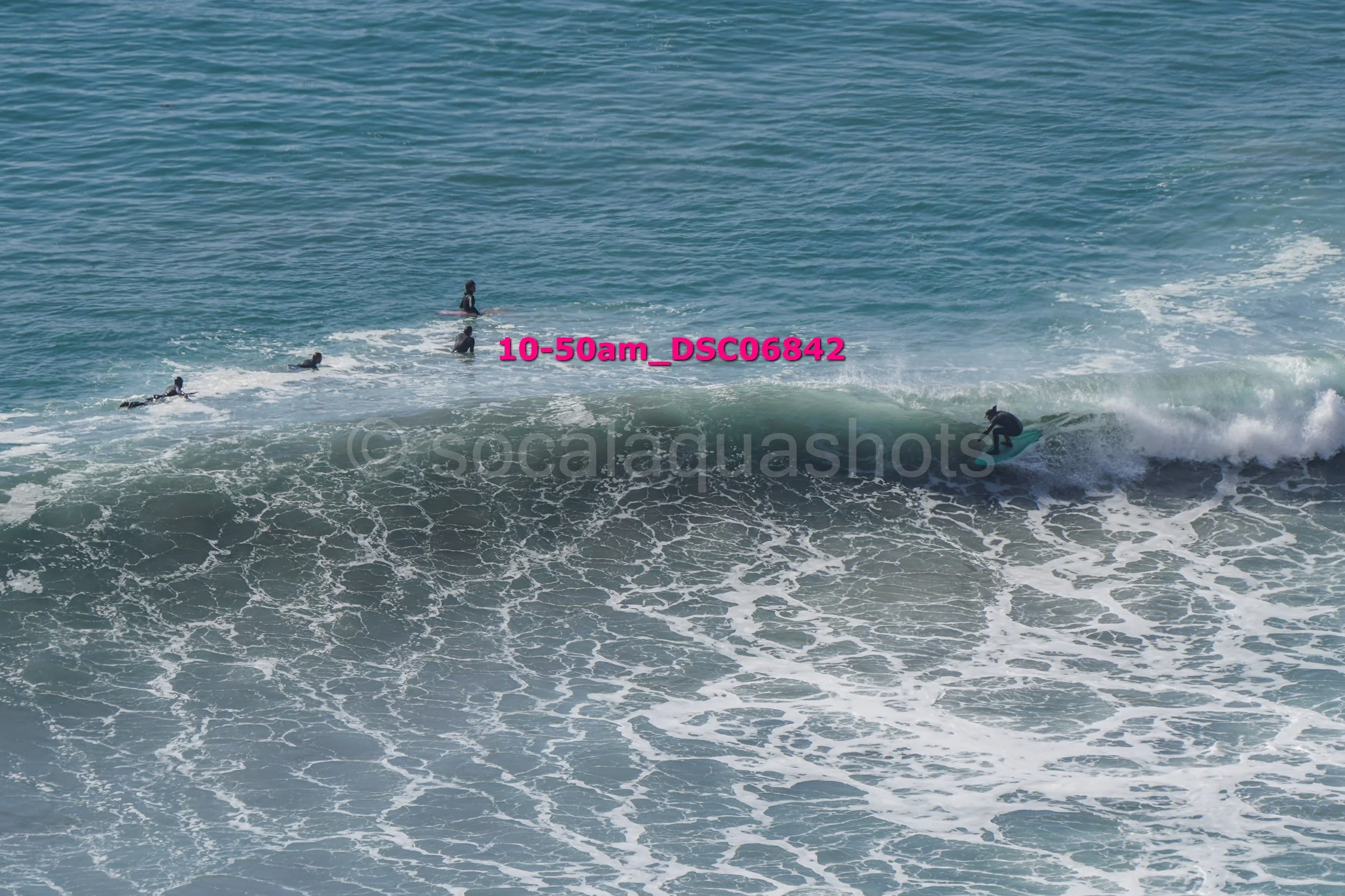 A person surfing on a wave with four other people swimming or floating nearby in the ocean.