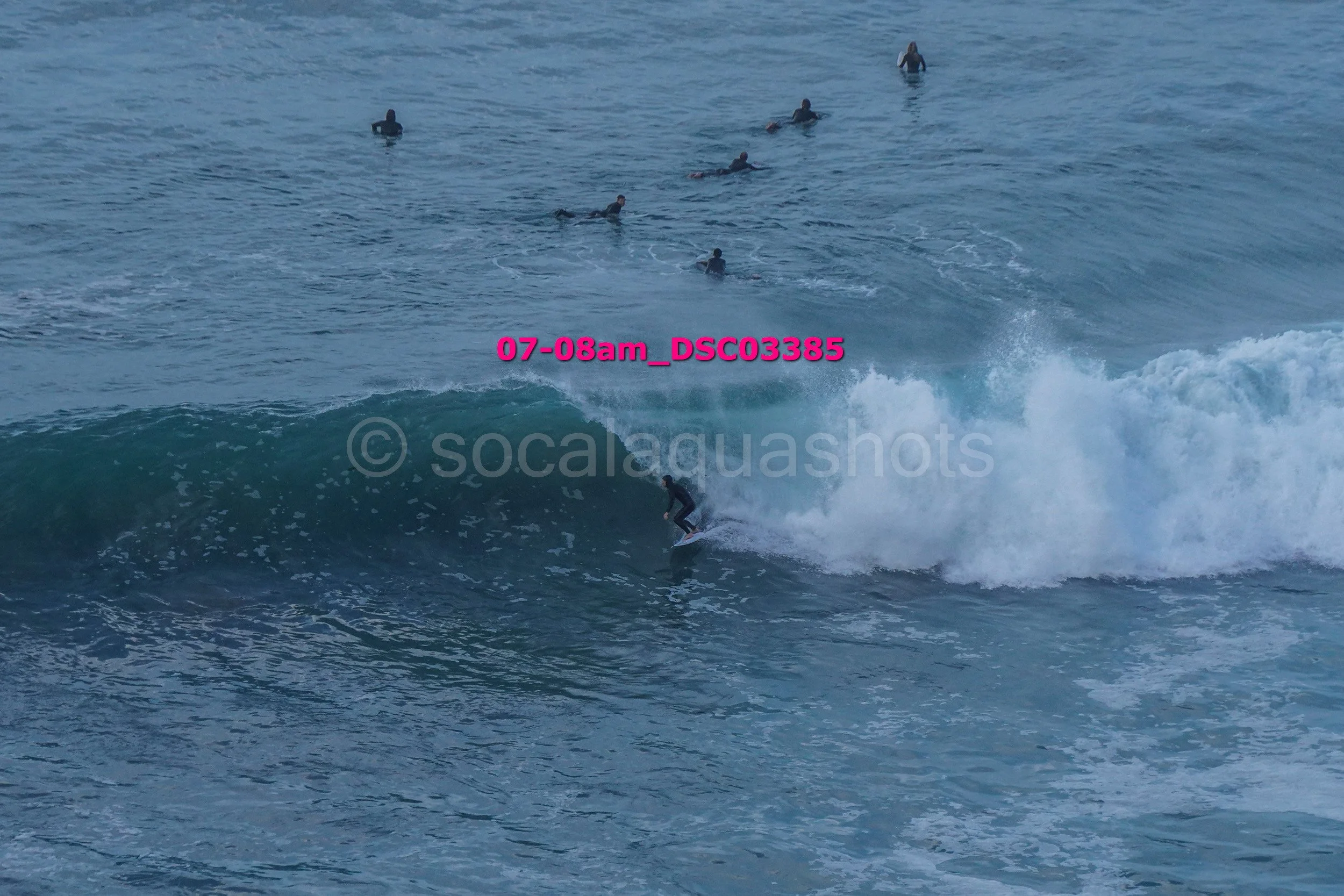 A person surfing on a wave in the ocean with several surfers in the water in the background.