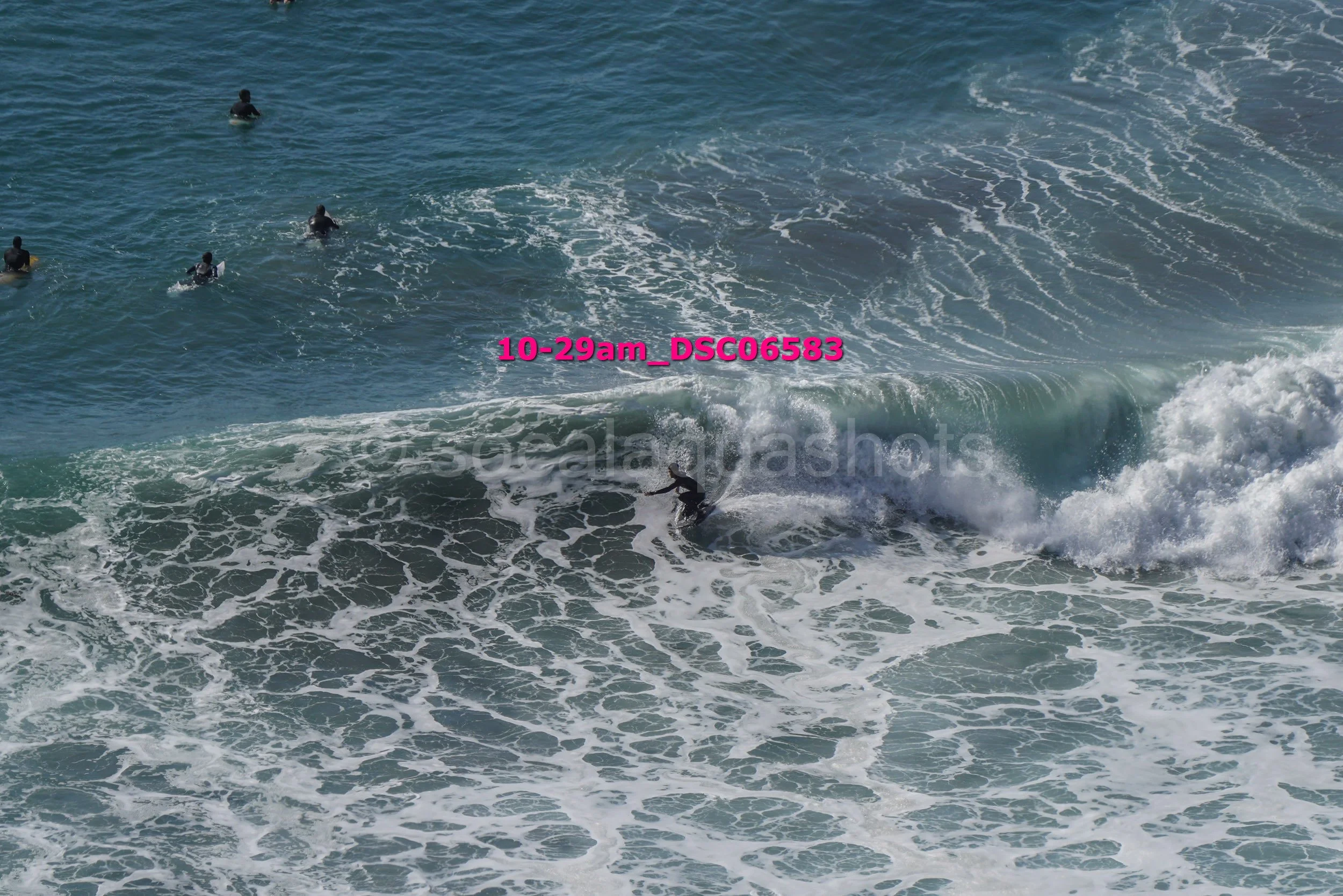 Surfer riding a wave, with four other surfers in the water nearby.