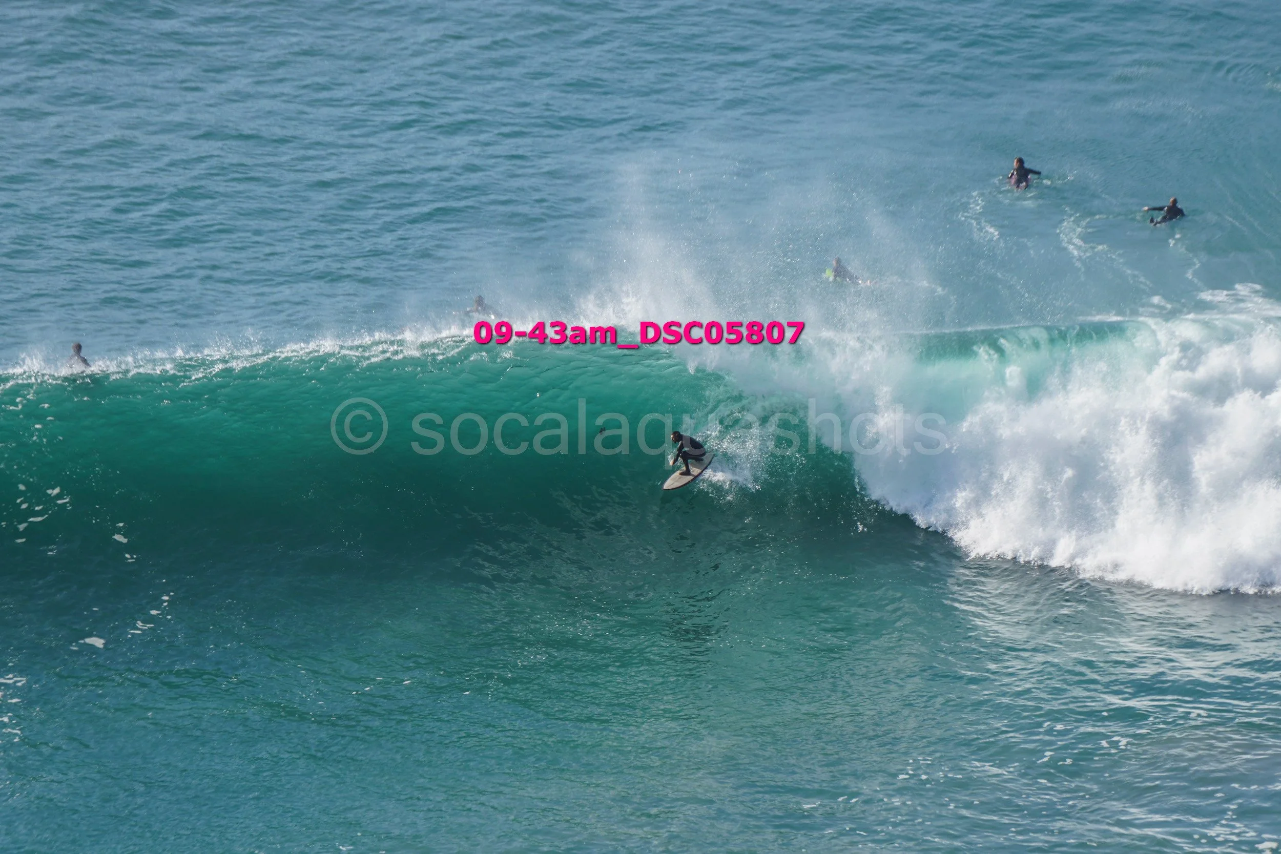 Surfer riding a large wave with several people in the water watching.