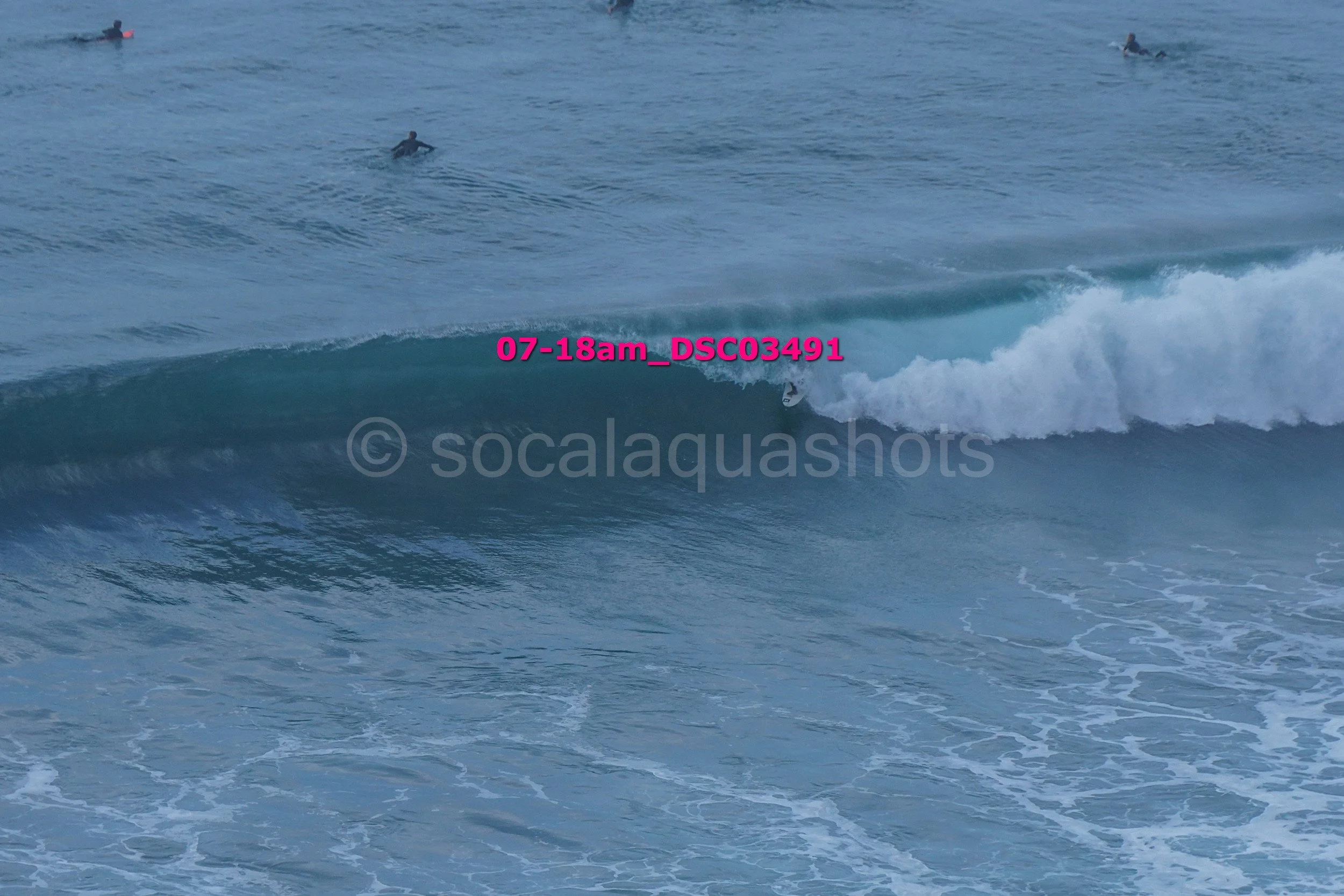 Surfer riding a wave at the beach, with several other surfers in the water in the background.