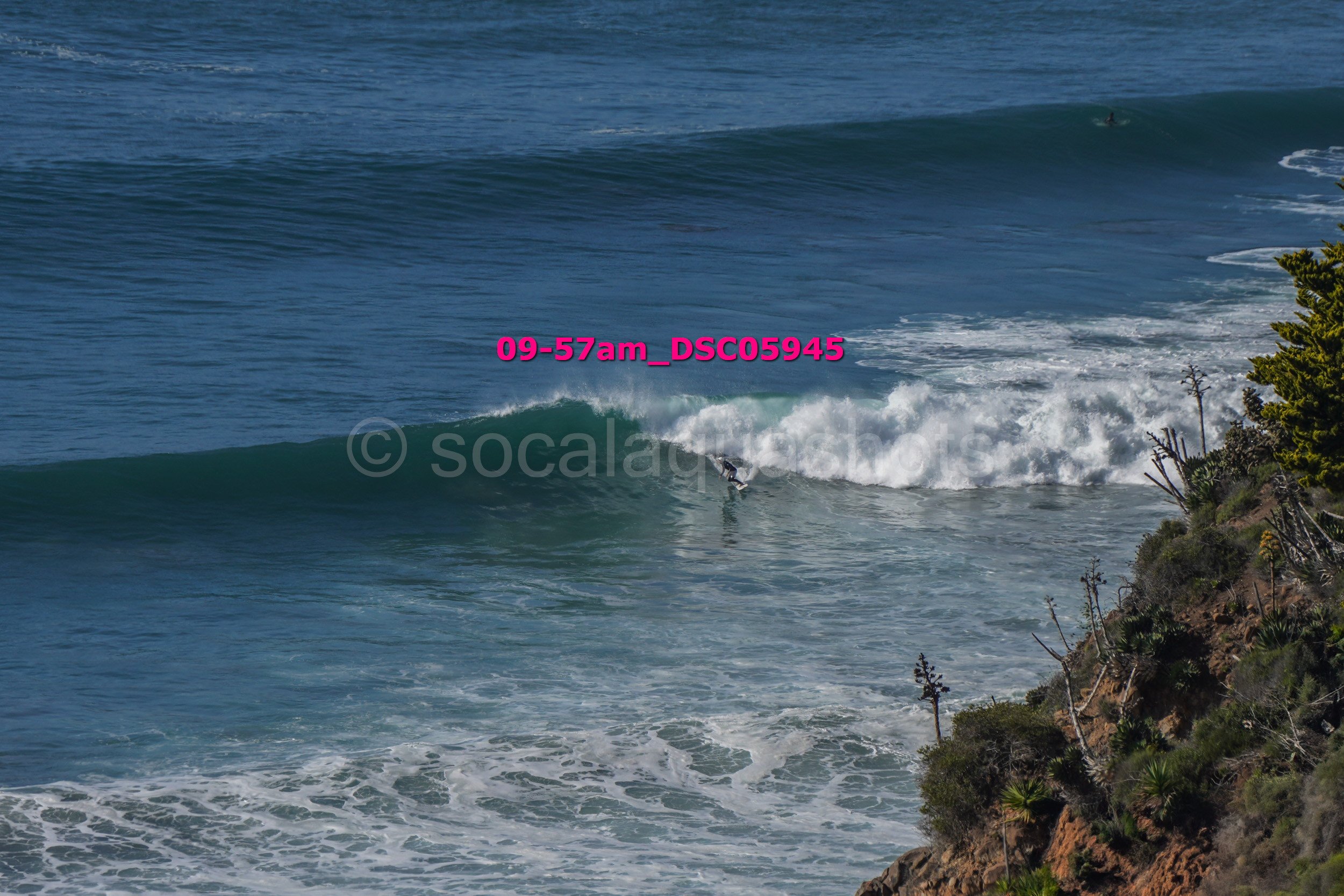 A person surfing on a wave near a rocky coastline with green vegetation.