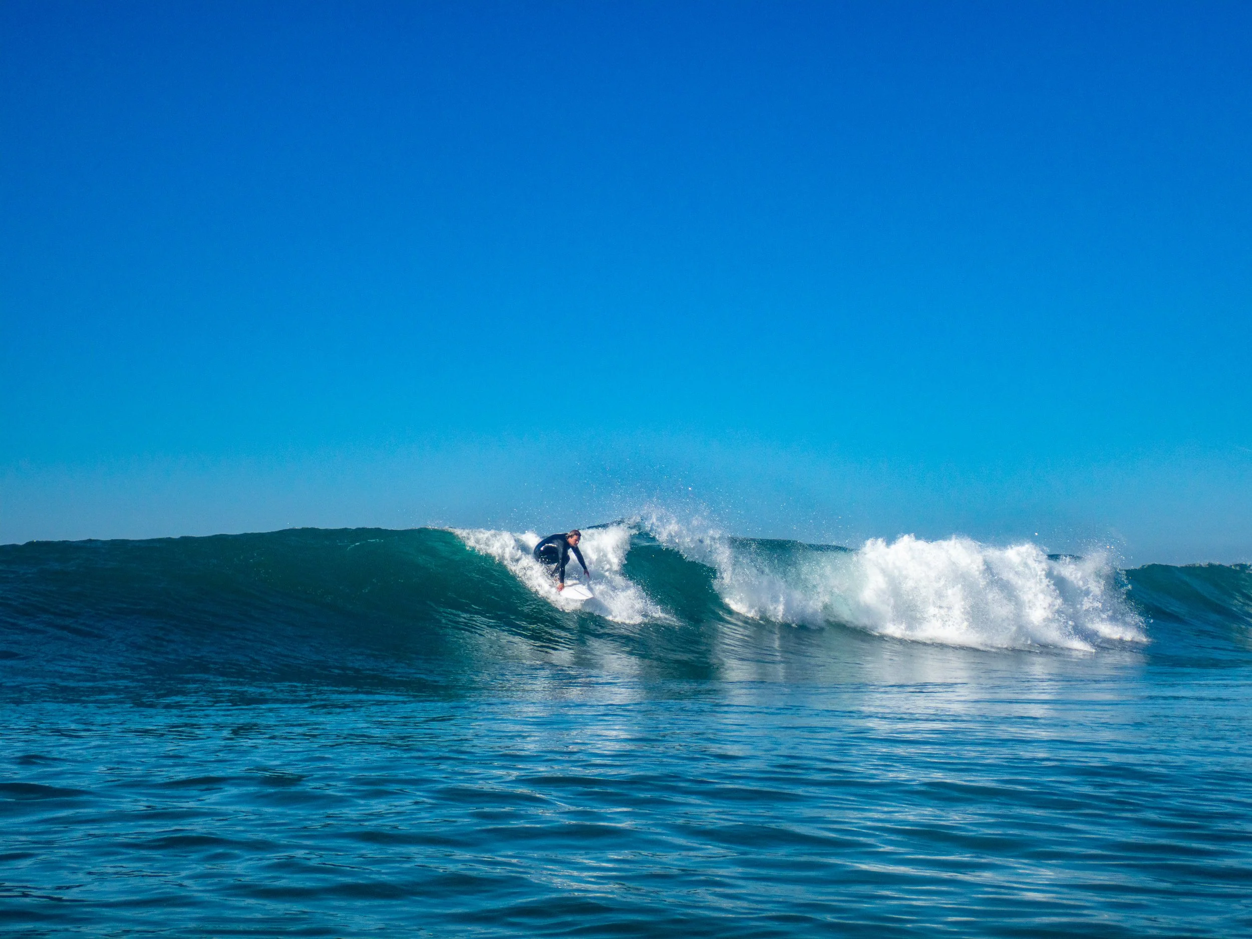 A person surfing on a wave in the ocean with clear blue sky above.