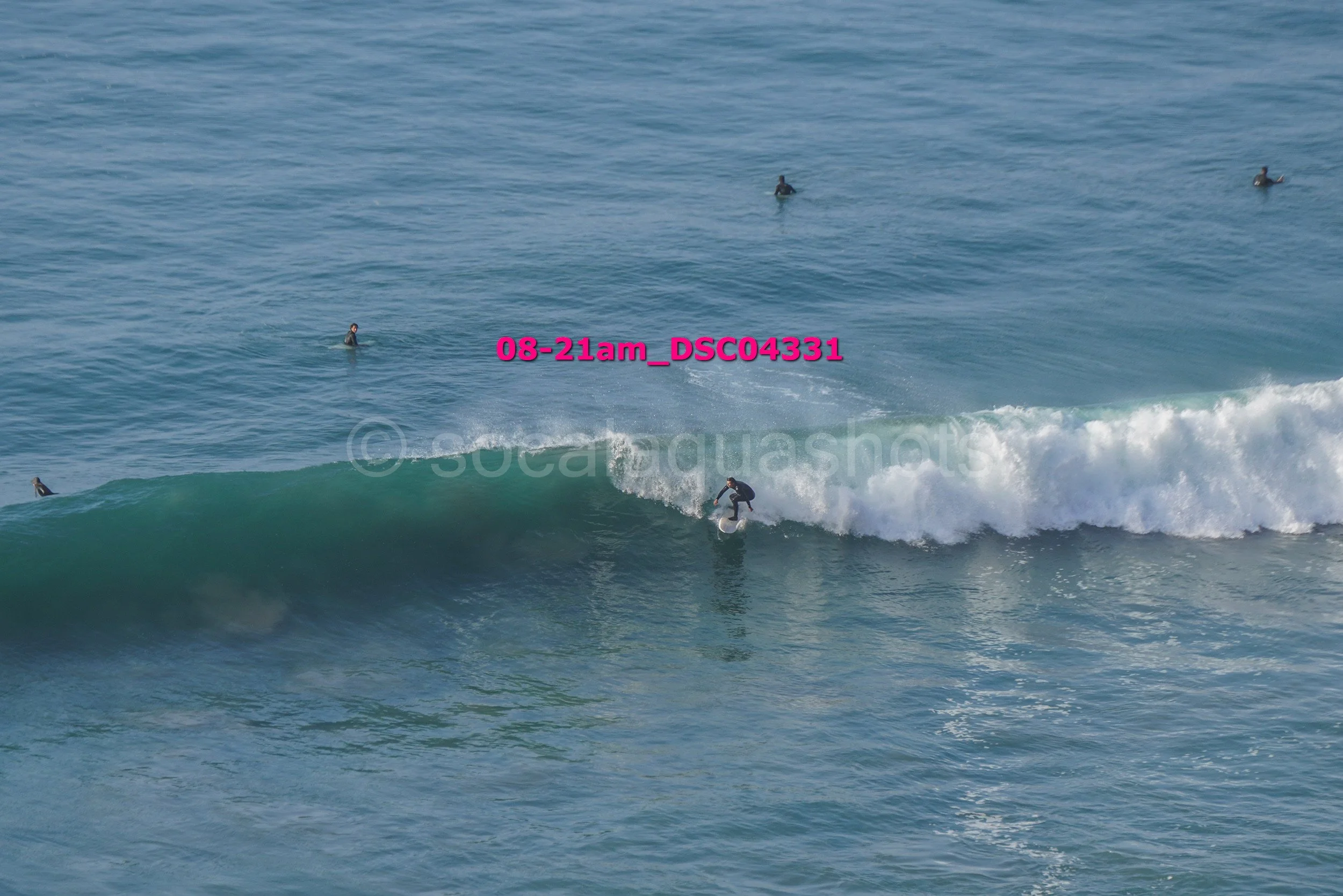 A surfer riding a wave in the ocean with several people in the water watching from a distance.