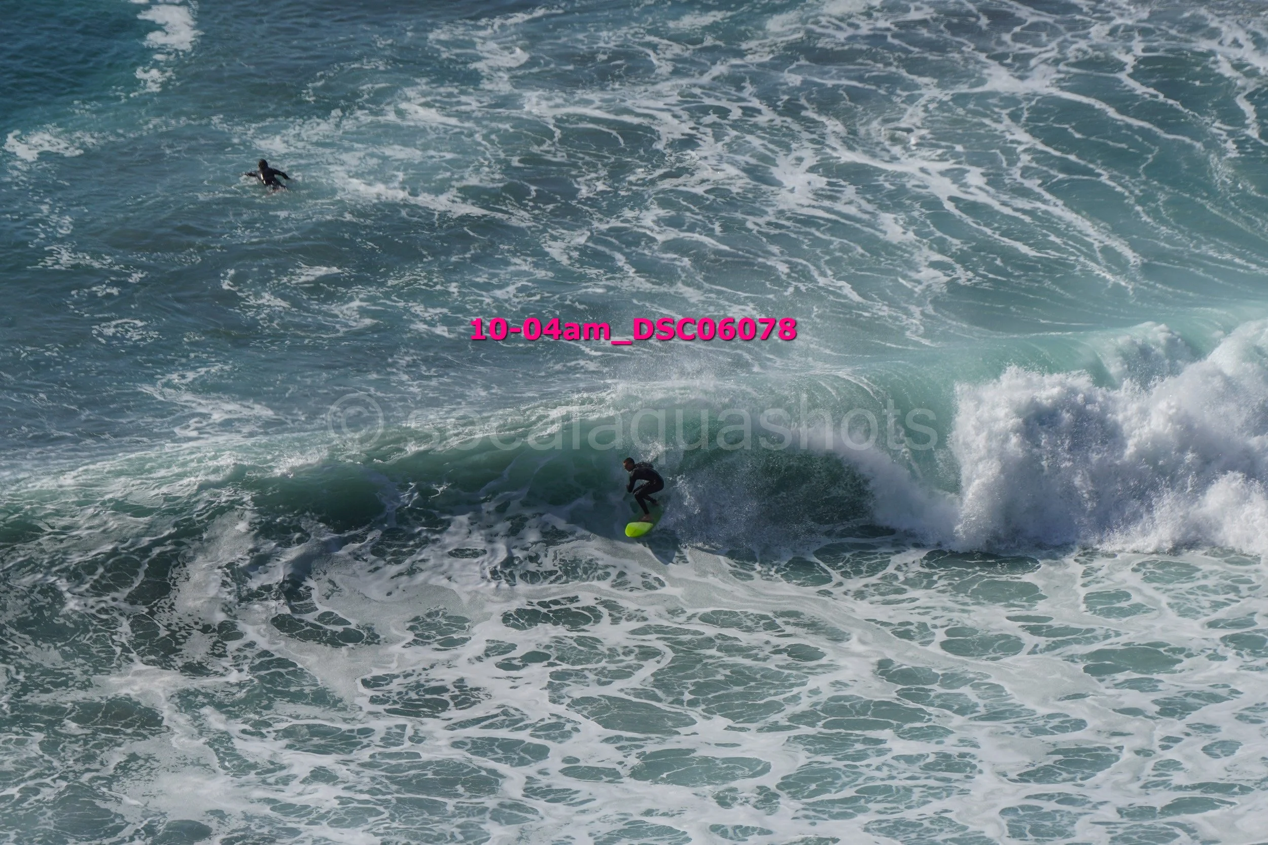 Surfer riding a wave with another surfer swimming in the background.