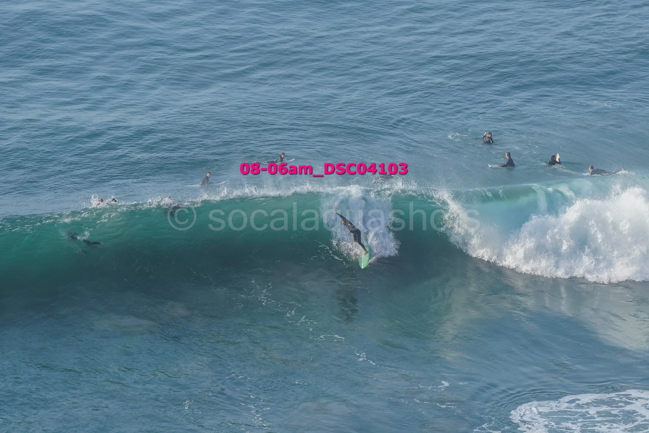 Surfer catching a wave in the ocean with multiple people in the water watching or waiting in the background.
