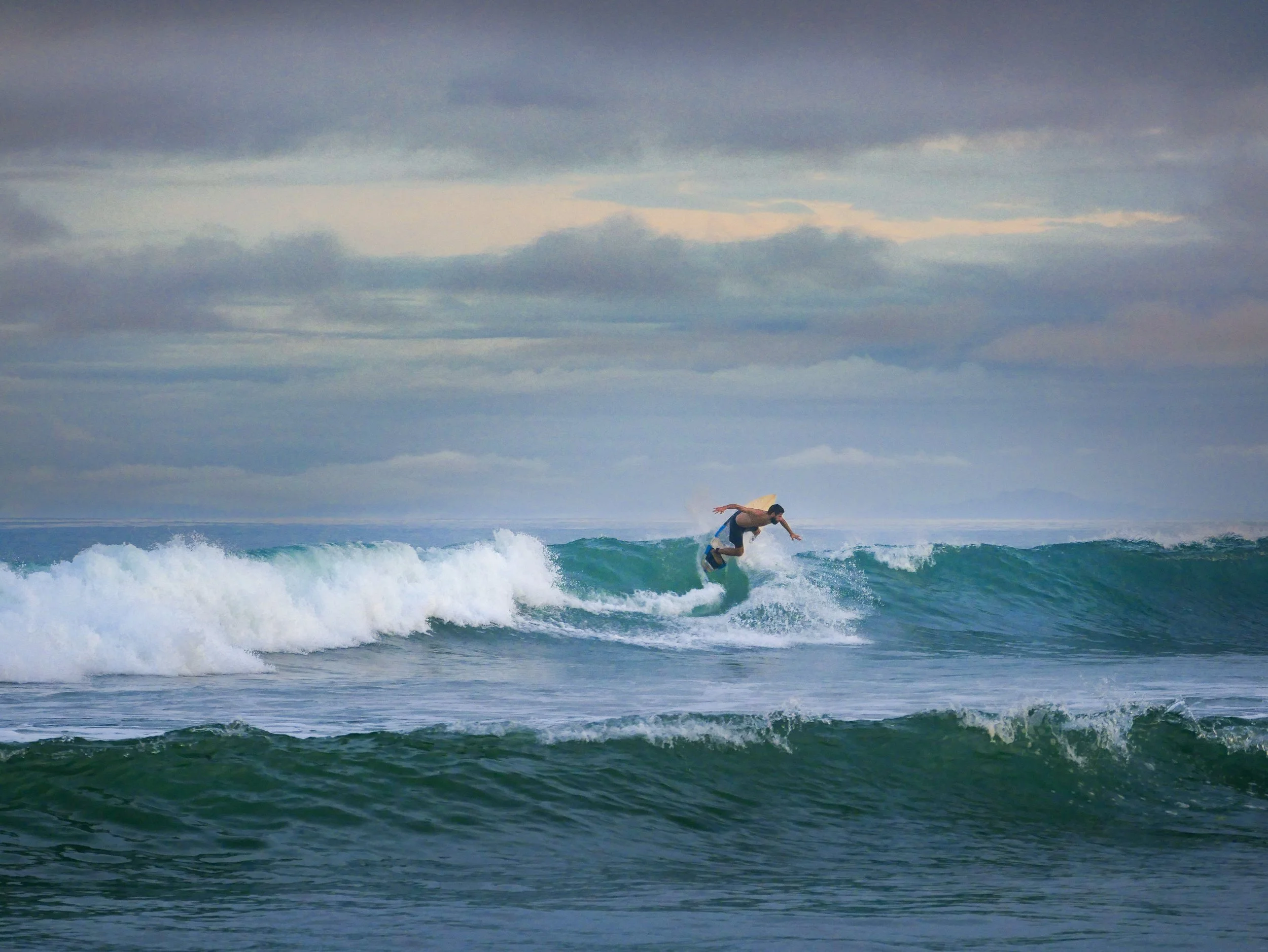 Surfer riding a wave on a cloudy day at sea