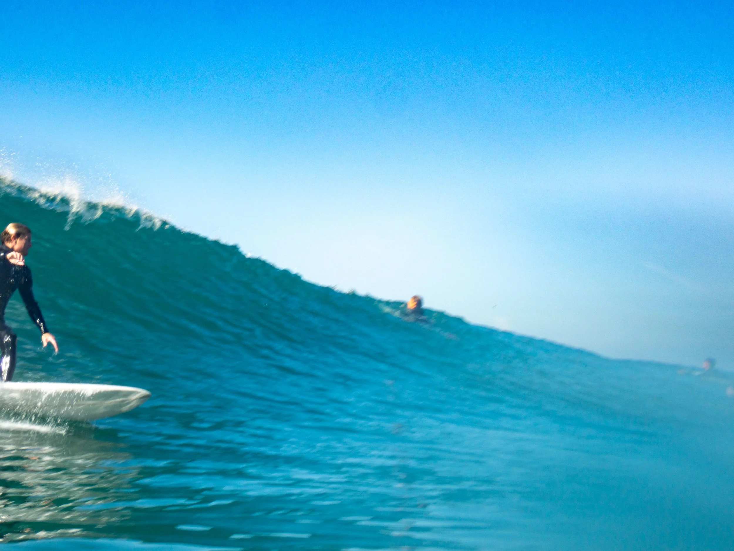 Person surfing on a wave in the ocean with a clear blue sky.