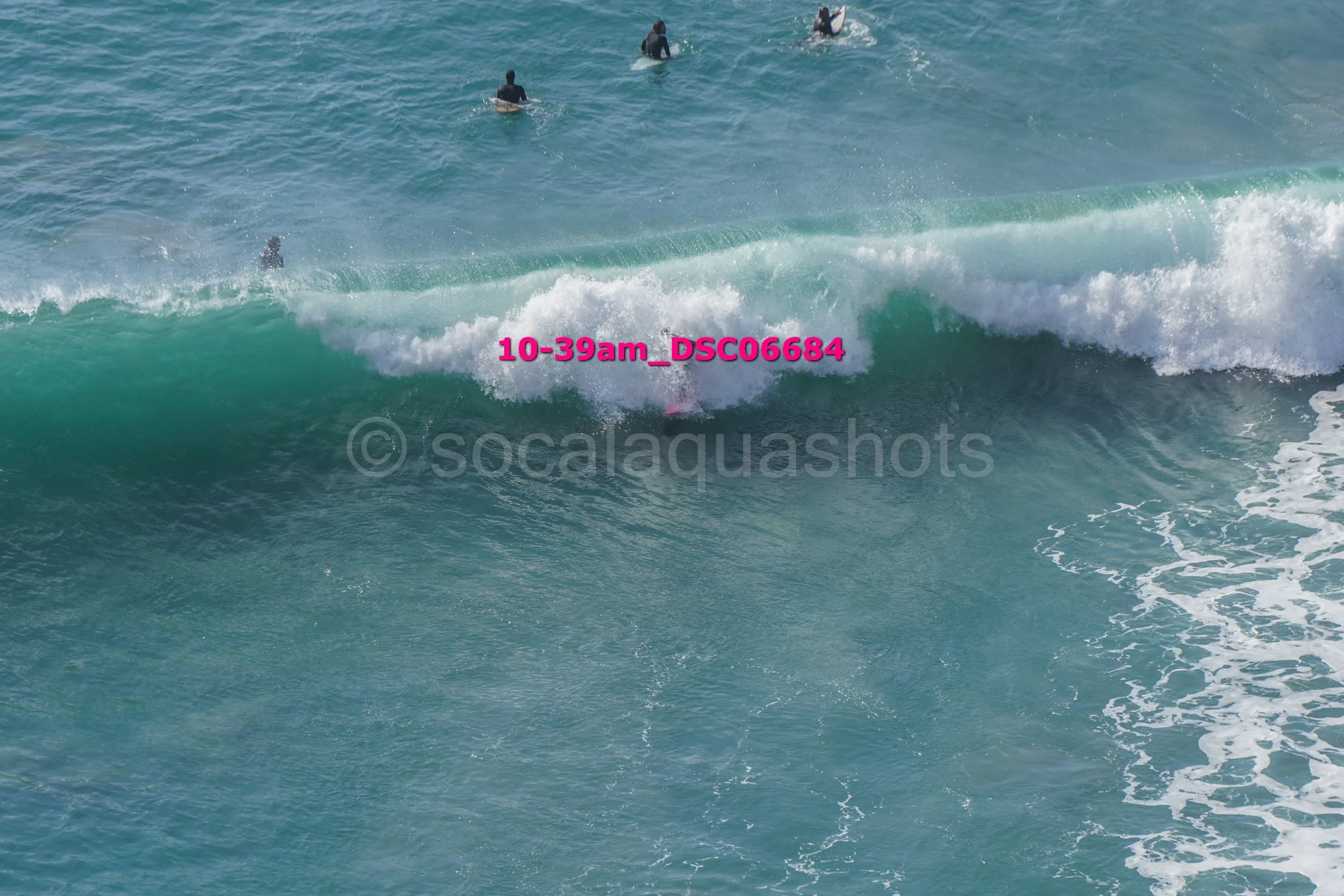 Multiple surfers waiting for waves in the ocean, with one surfer catching a wave in the foreground.
