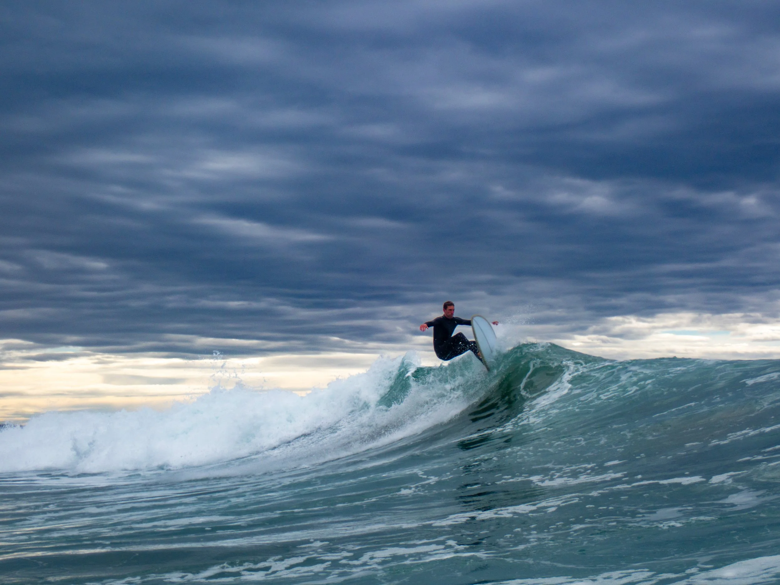 A person surfing on a wave in an ocean under a cloudy sky.