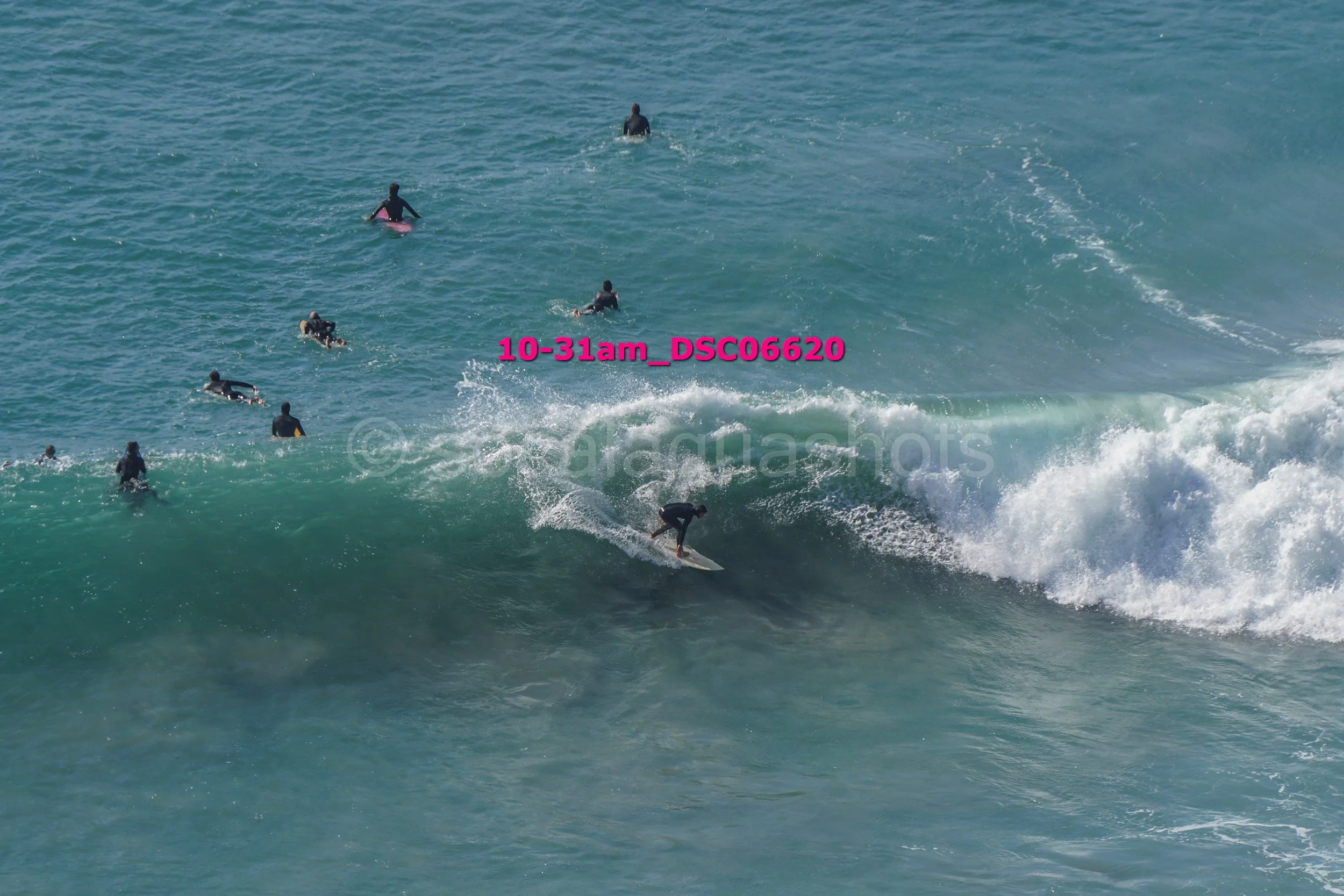 Surfer riding a wave with several swimmers and surfers in the water in the background.