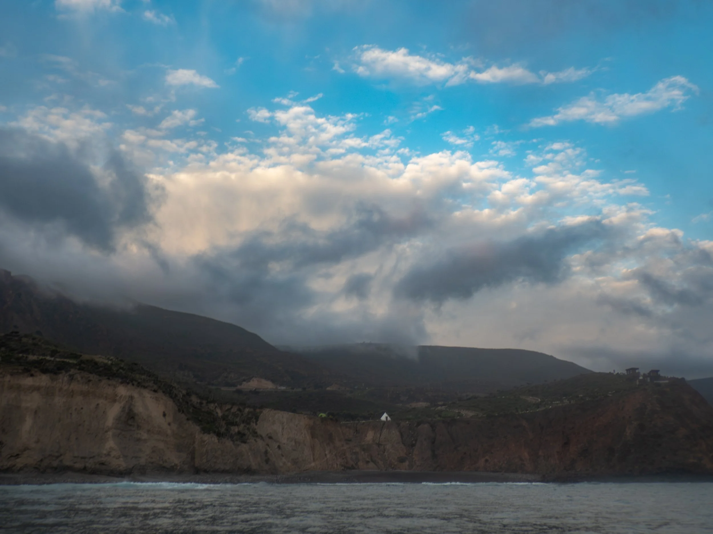 Cloudy sky over rugged coastline with cliffs and buildings in the distance.