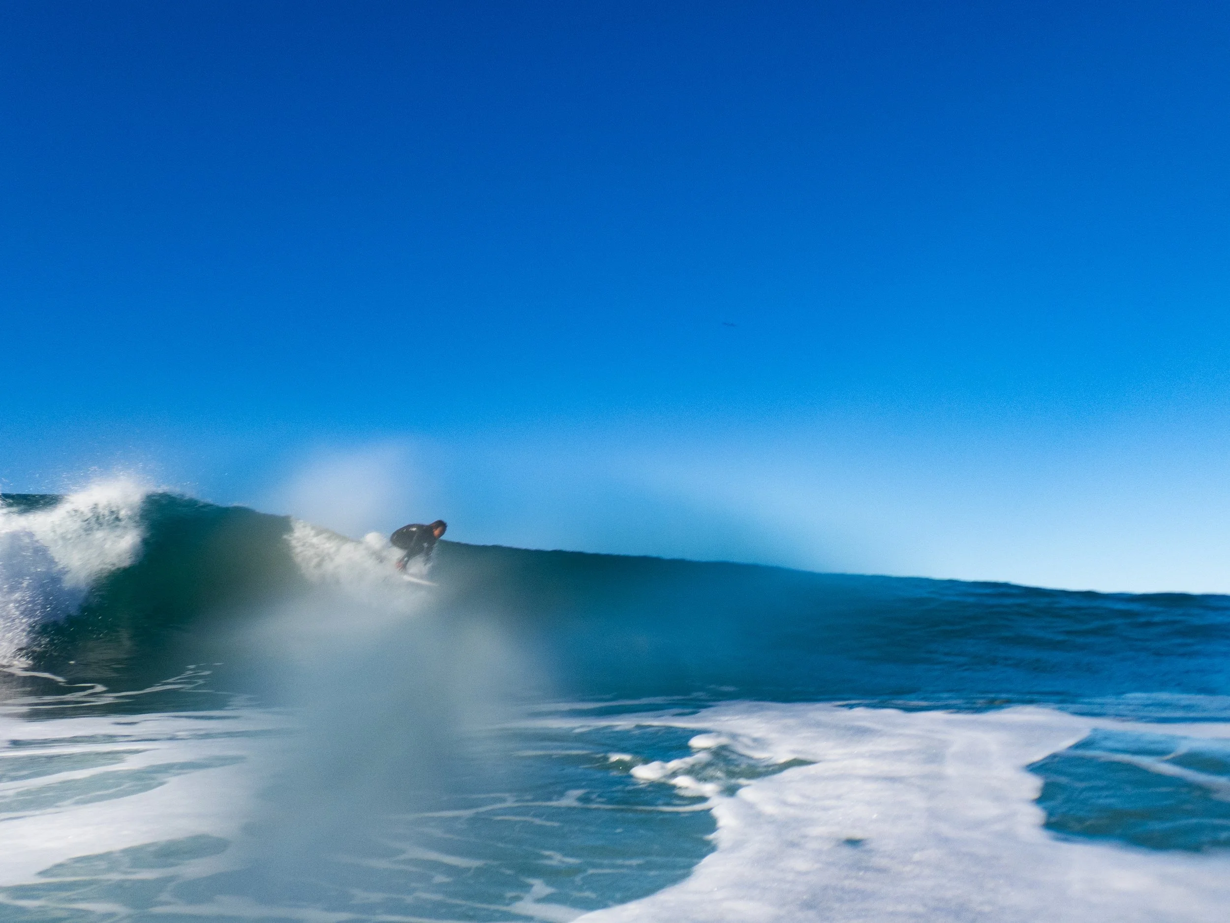 A person surfing on a wave in the ocean under a clear blue sky.