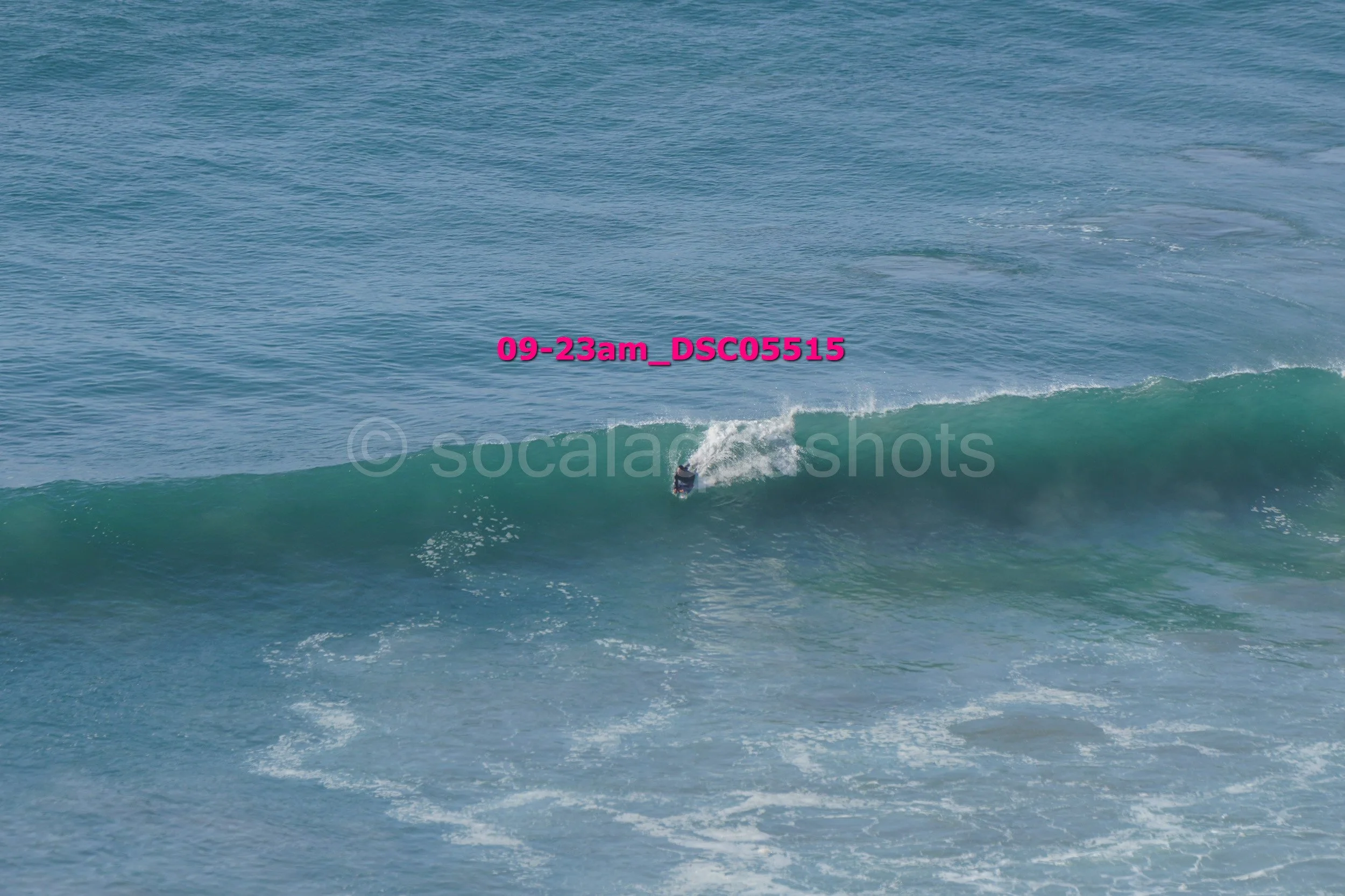 A person surfing on a wave in the ocean with the timestamp '09-23am_DSC05515' overlaid.