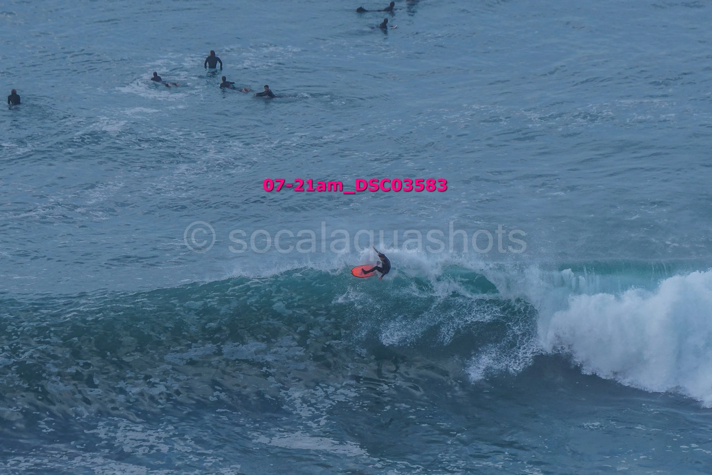 A person surfing on a wave with several people in the water in the background