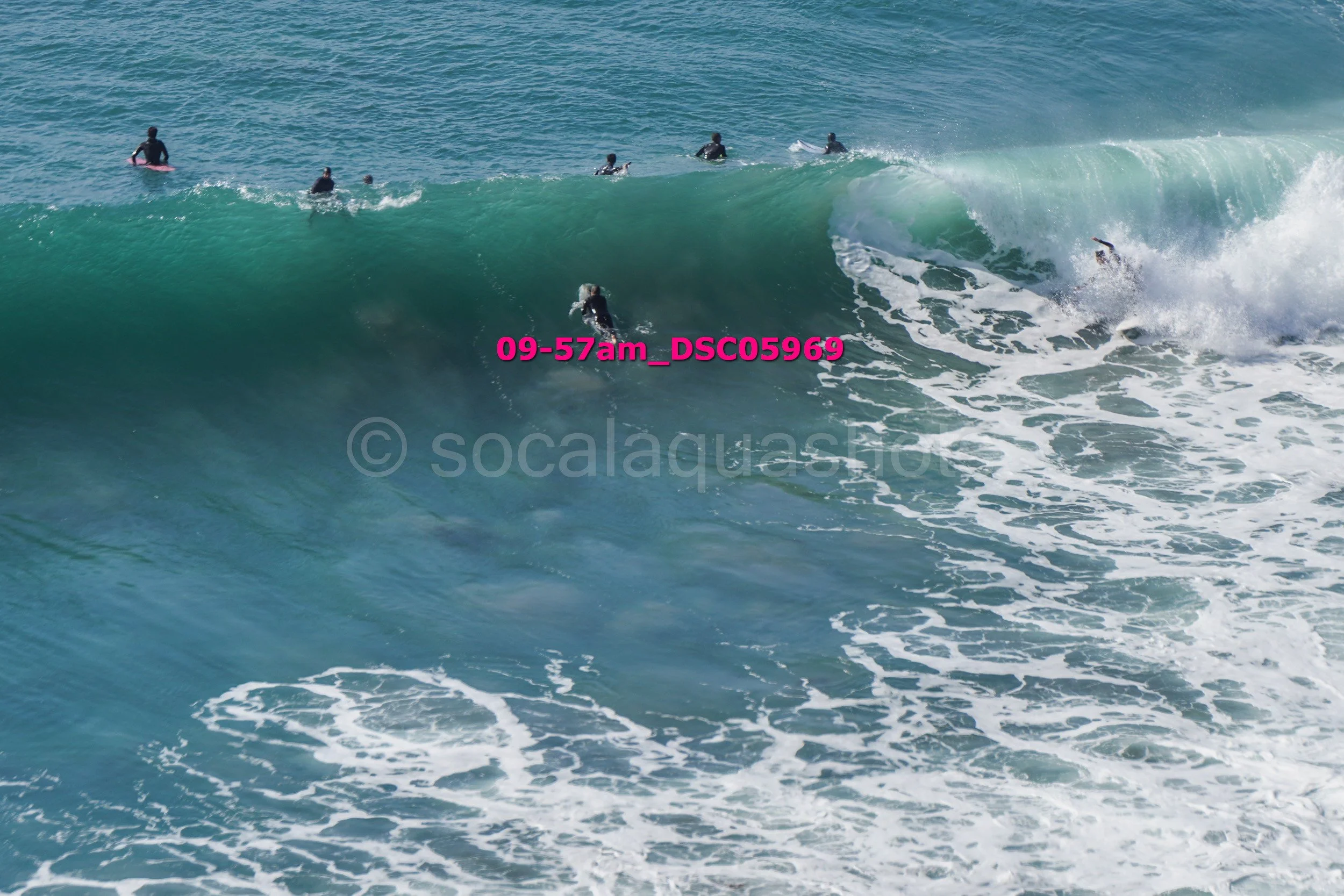 Multiple surfers in wetsuits riding and paddling on large ocean waves at a beach.
