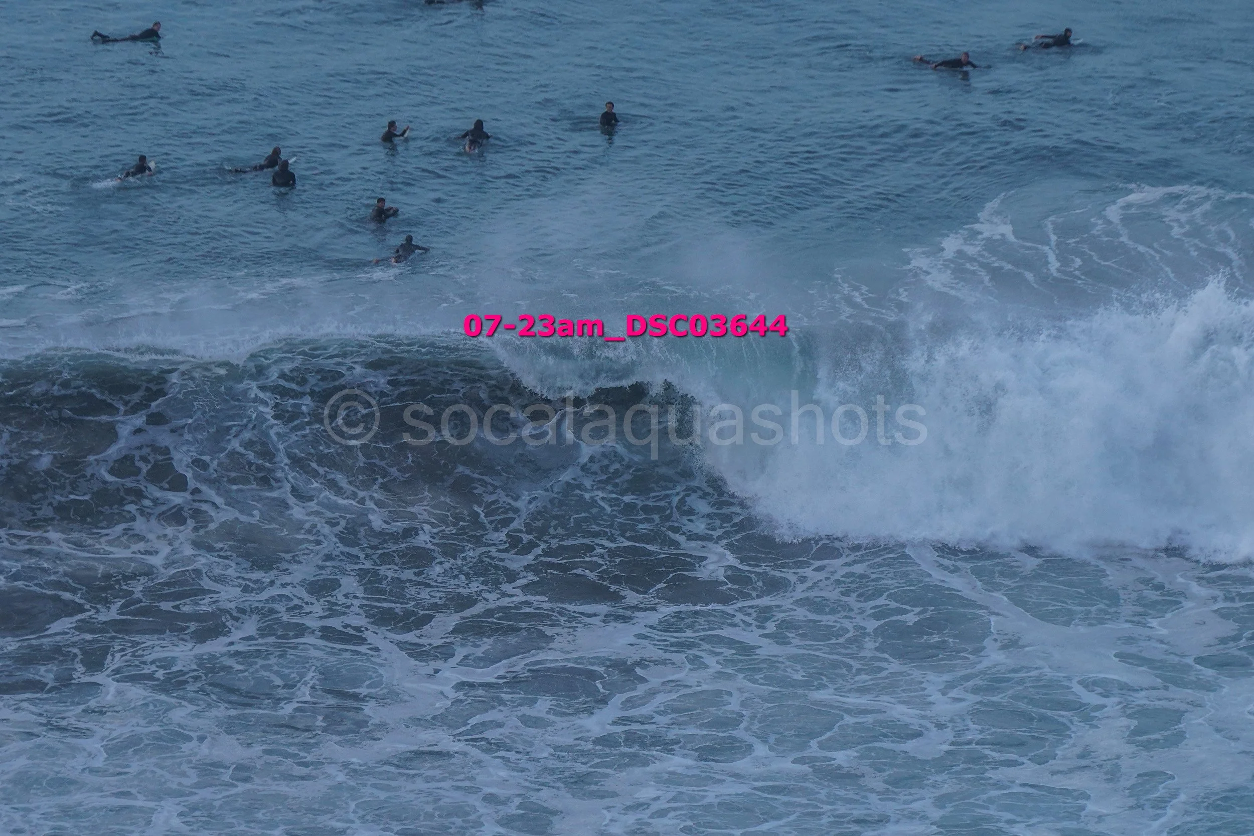 A group of people swimming and surfing in the ocean with waves crashing.