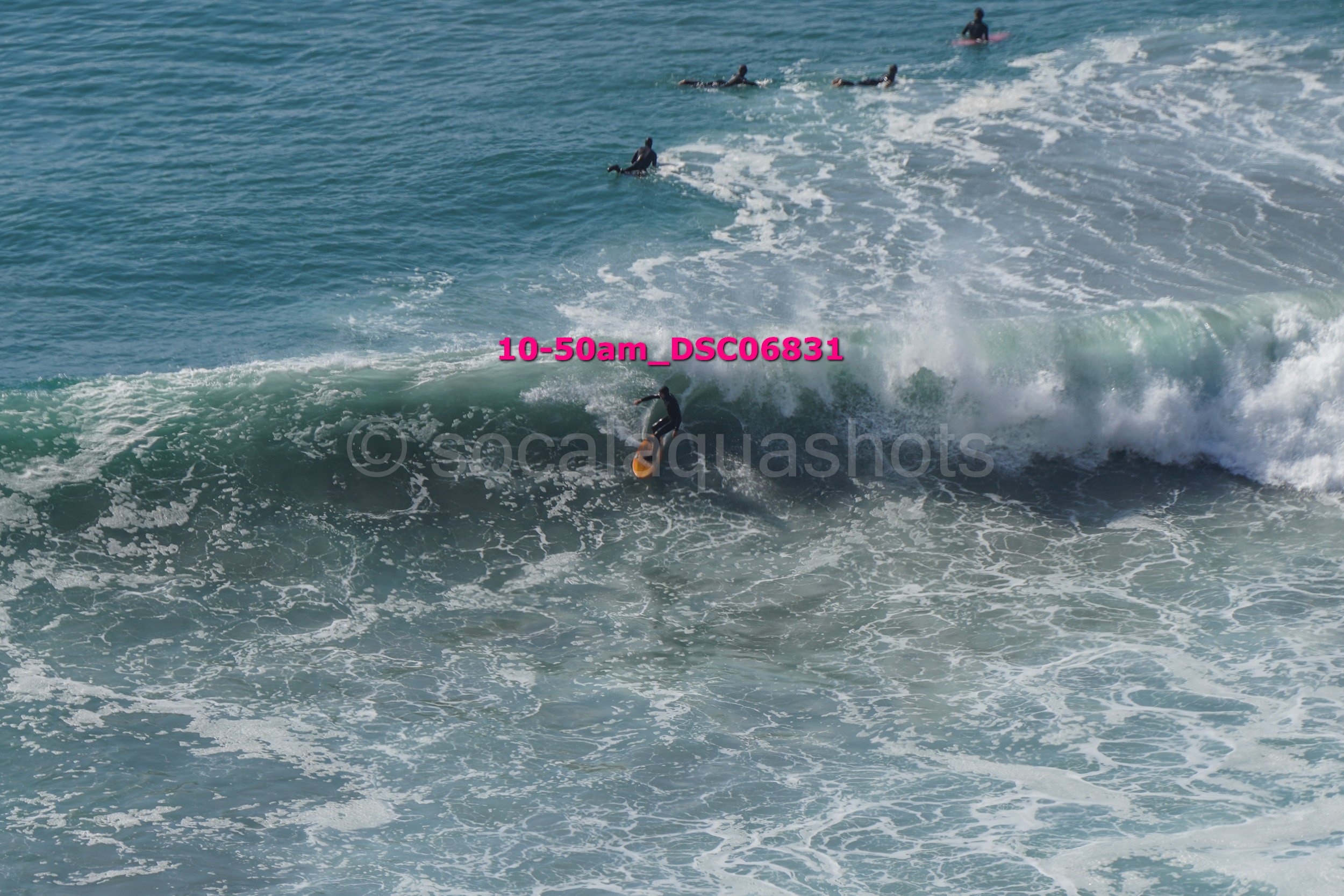 Person surfing on a wave in the ocean with several other surfers in the background.