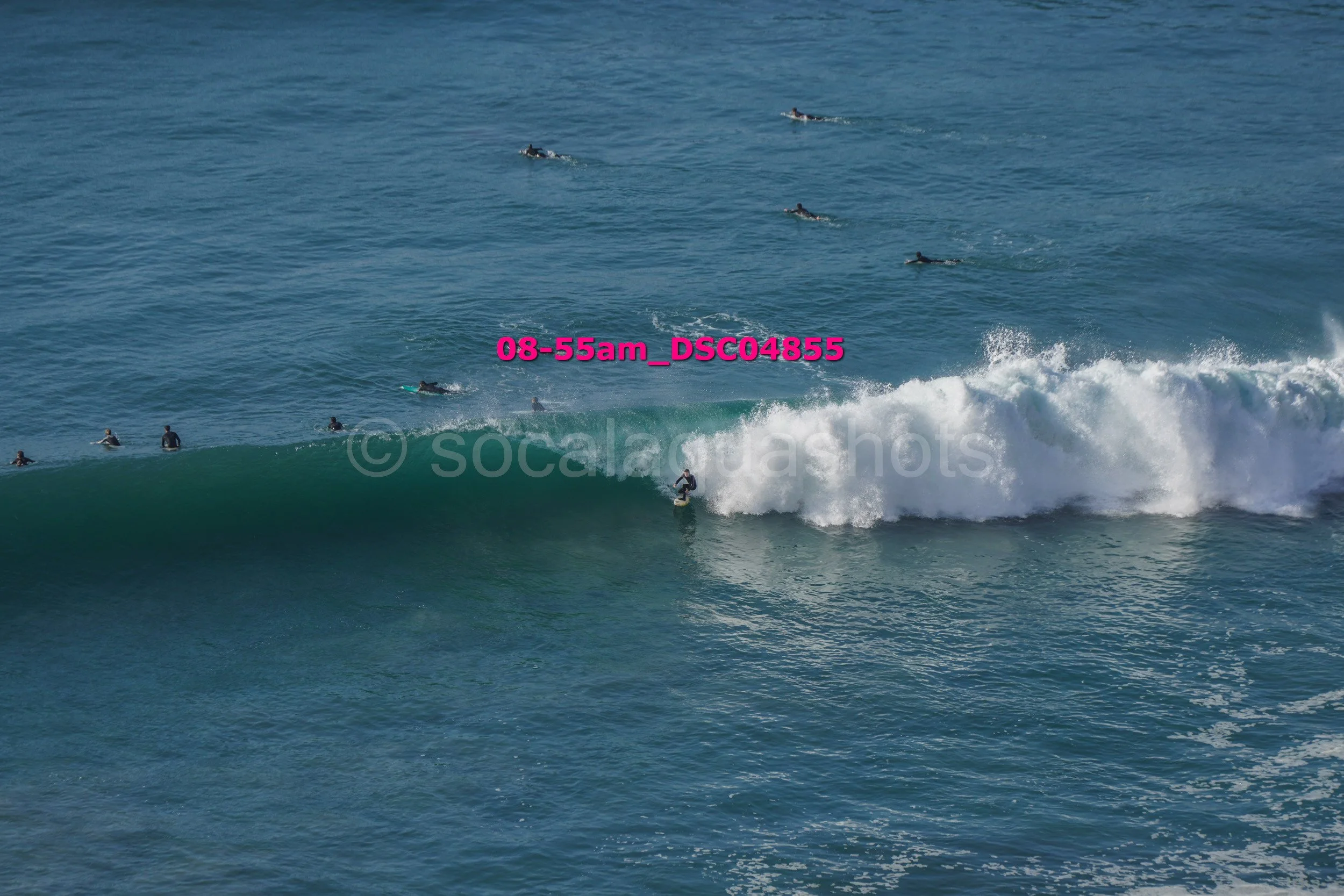 Surfer riding a wave with multiple surfers in the water in the background.