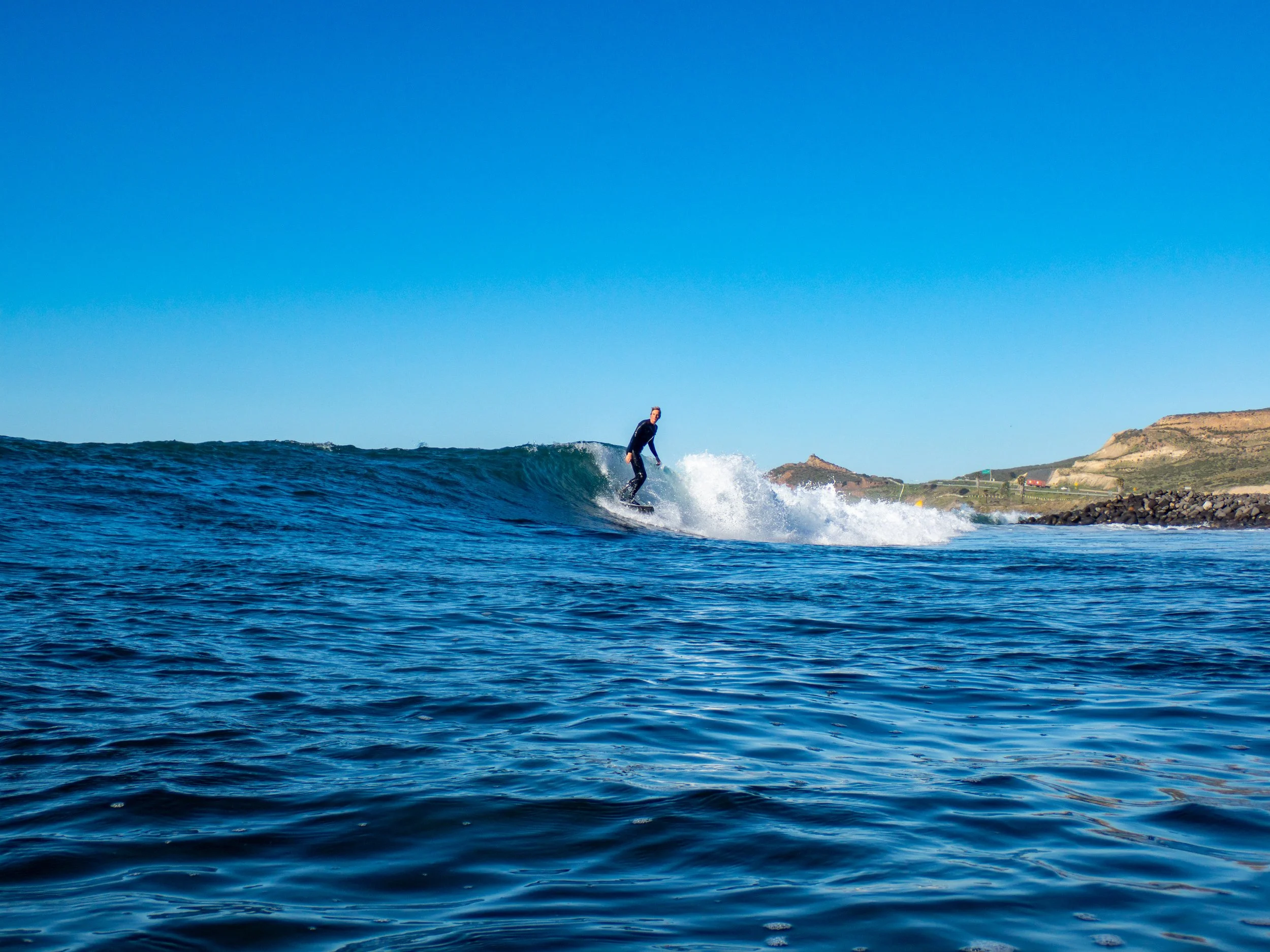 A person surfing on a wave in the ocean with a clear blue sky.