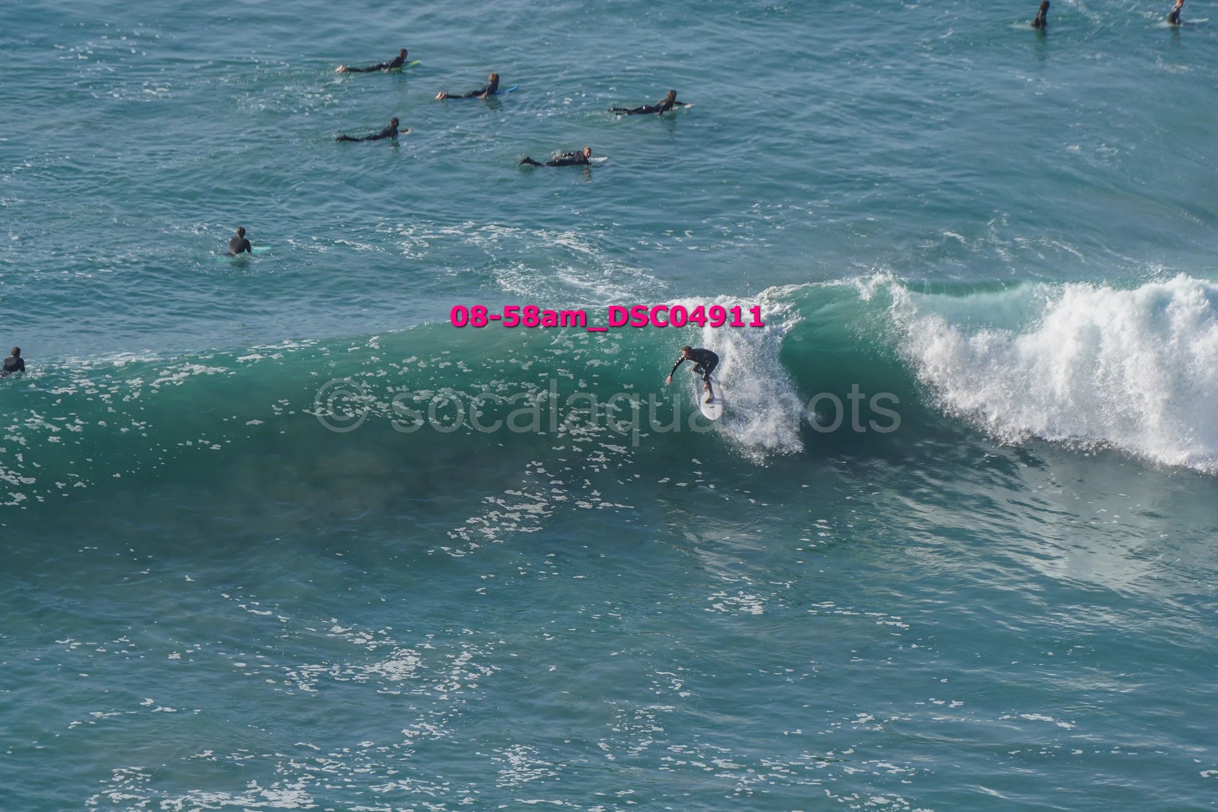 Surfer riding a wave with several people in the water in the background.