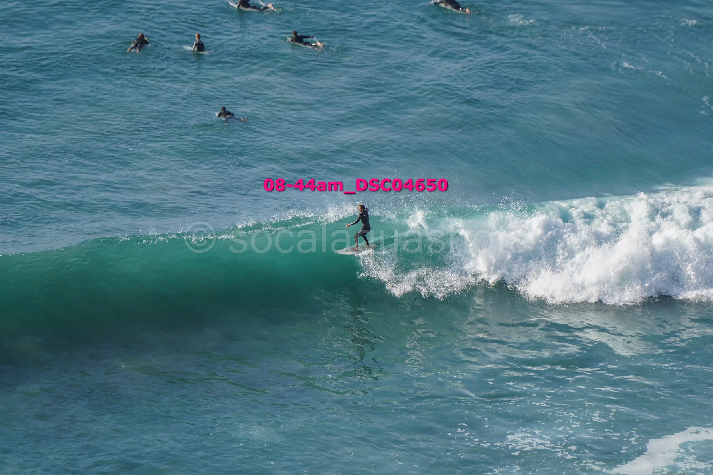 A person surfing on a wave while several others are swimming in the ocean behind.