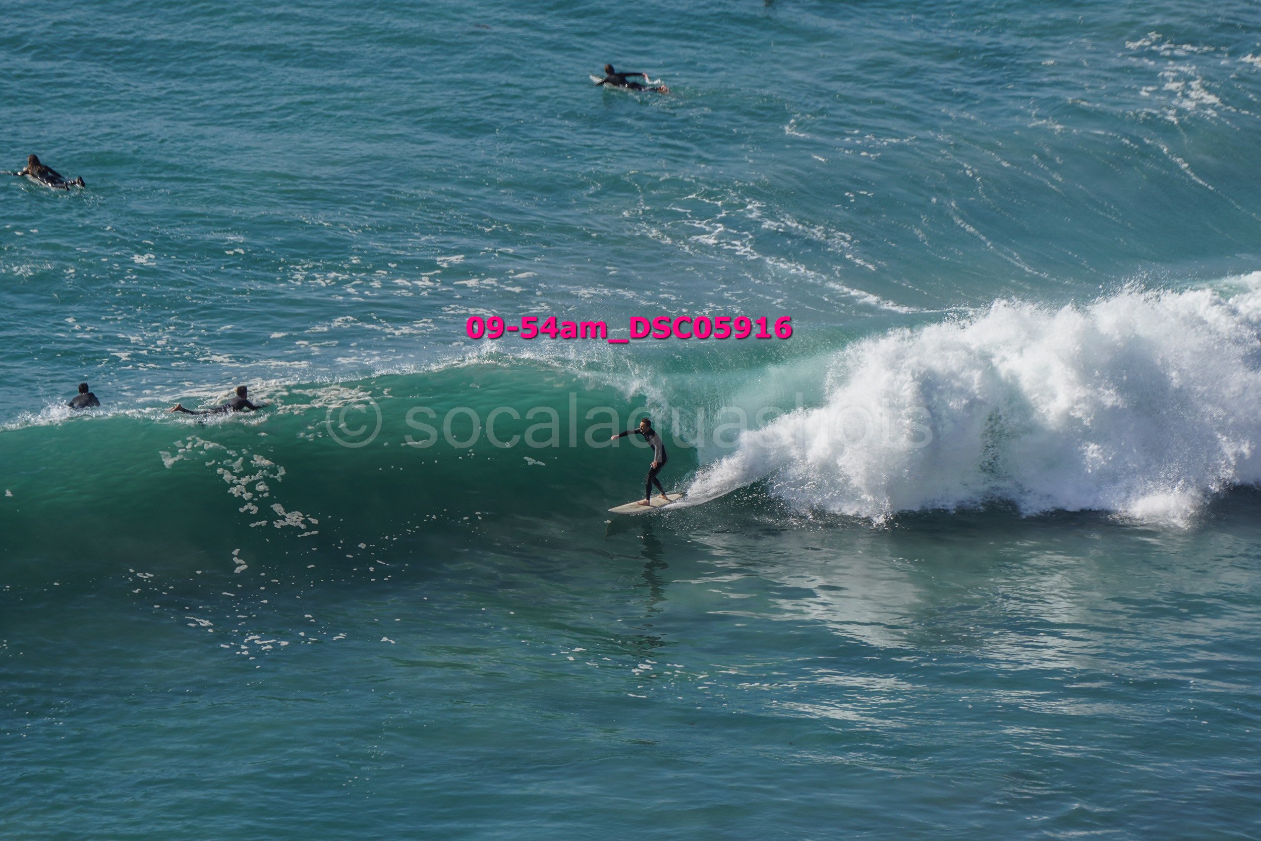 A person surfing on a wave in the ocean with several other surfers in the water around them.