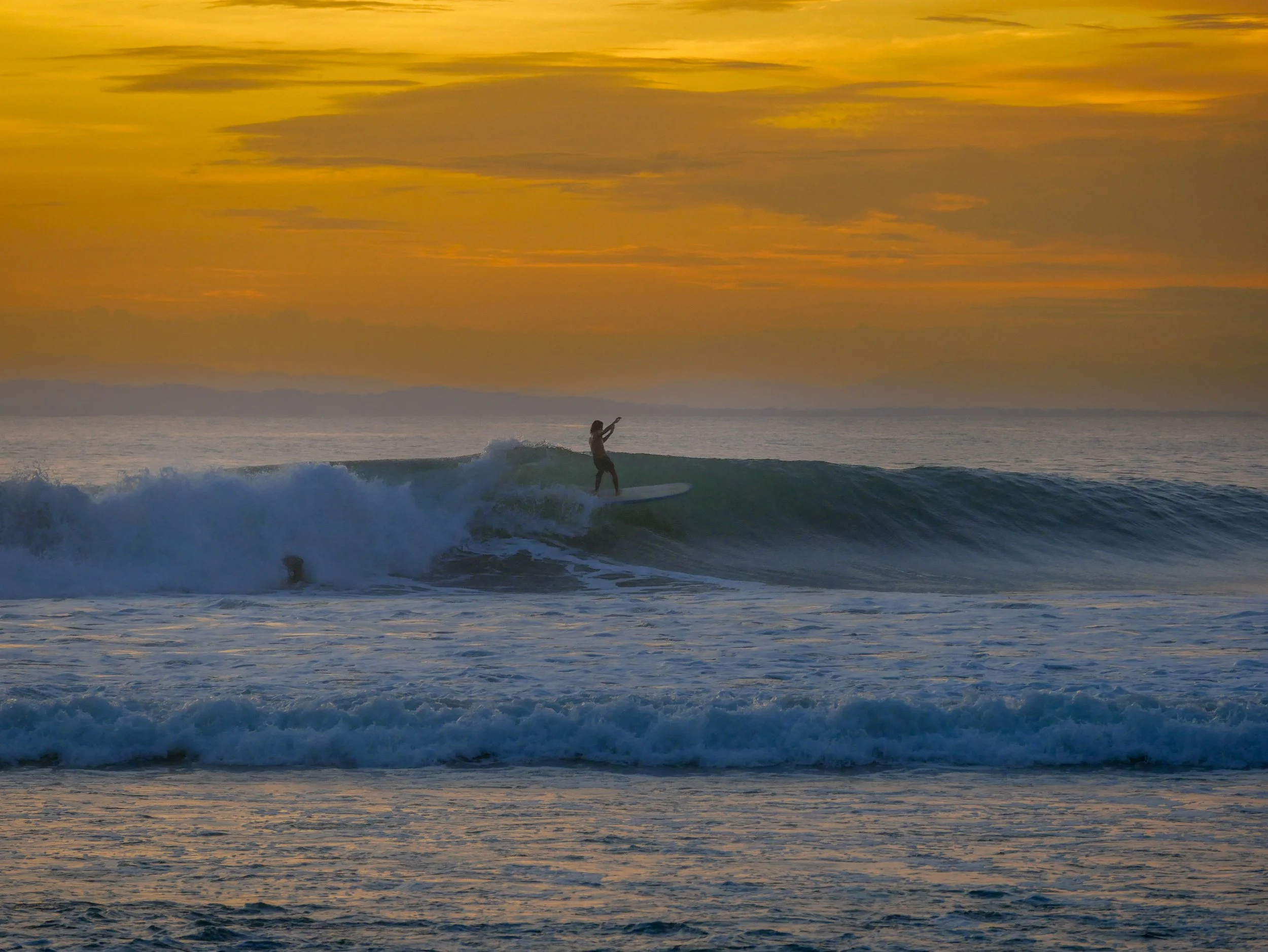 Surfer riding a wave at sunset with golden sky