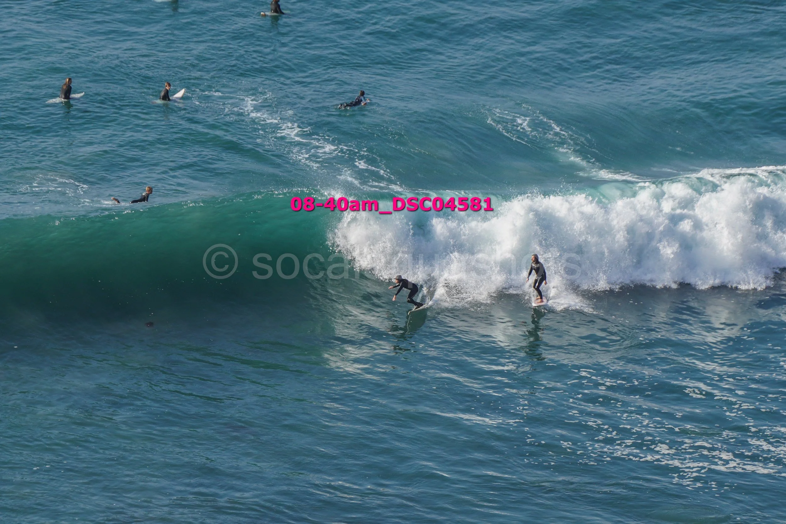 Multiple surfers riding and sitting on waves in the ocean during daytime.