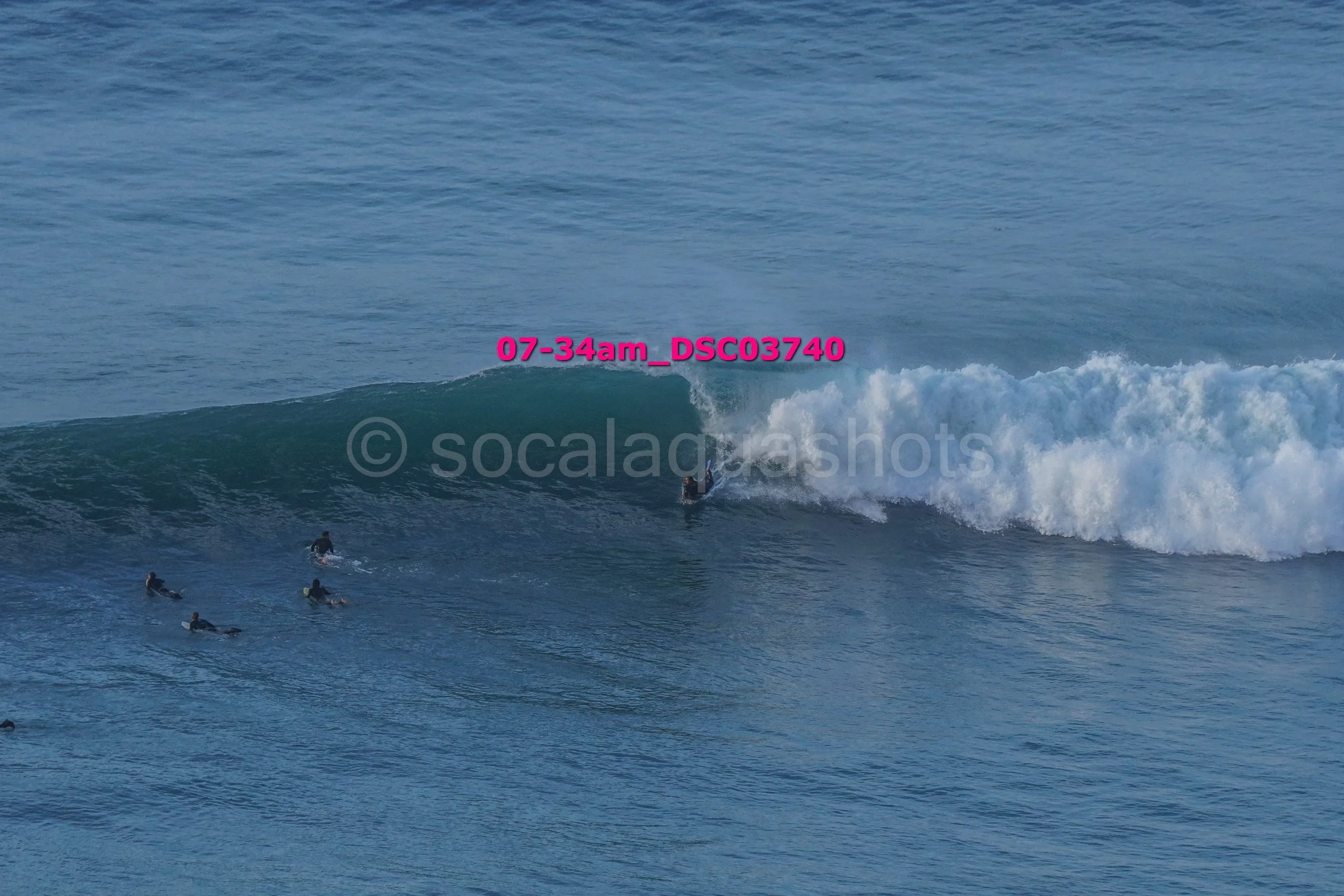 Surfer riding a wave with several other surfers waiting in the water at a beach.