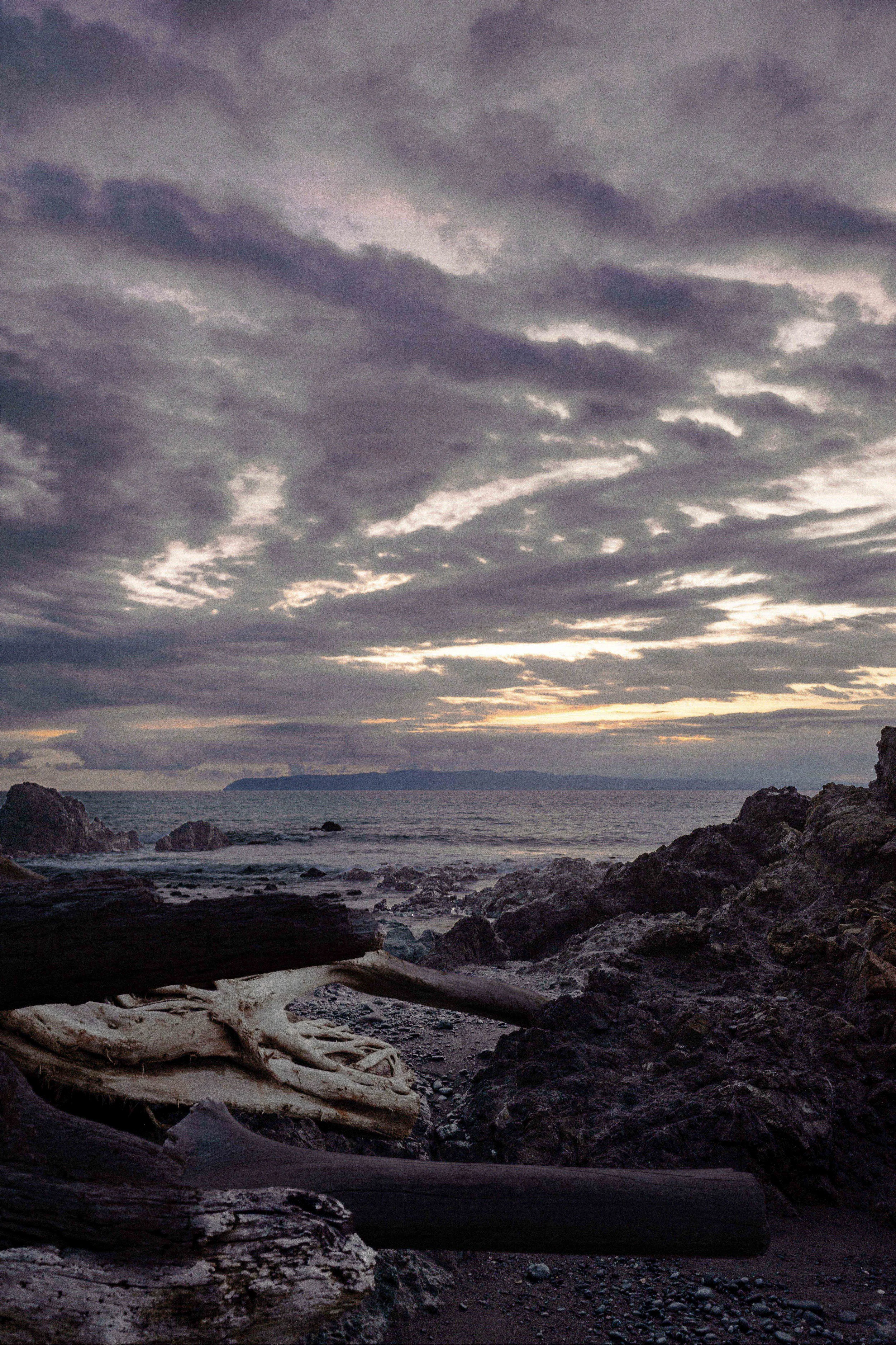 A rocky beach at dusk with dark clouds in the sky and a distant landmass visible on the horizon.