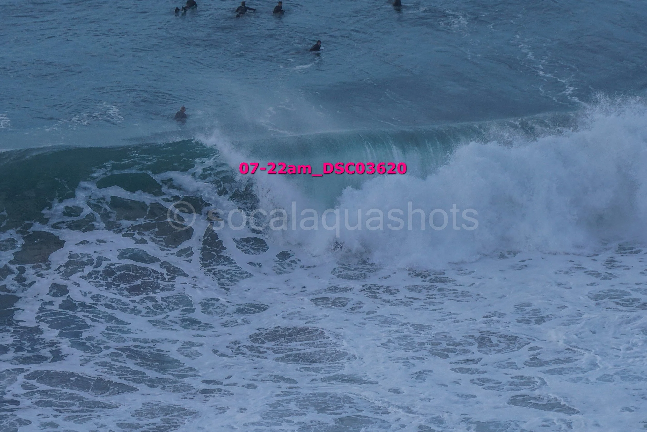 Waves crashing on the ocean with several surfers in the background.