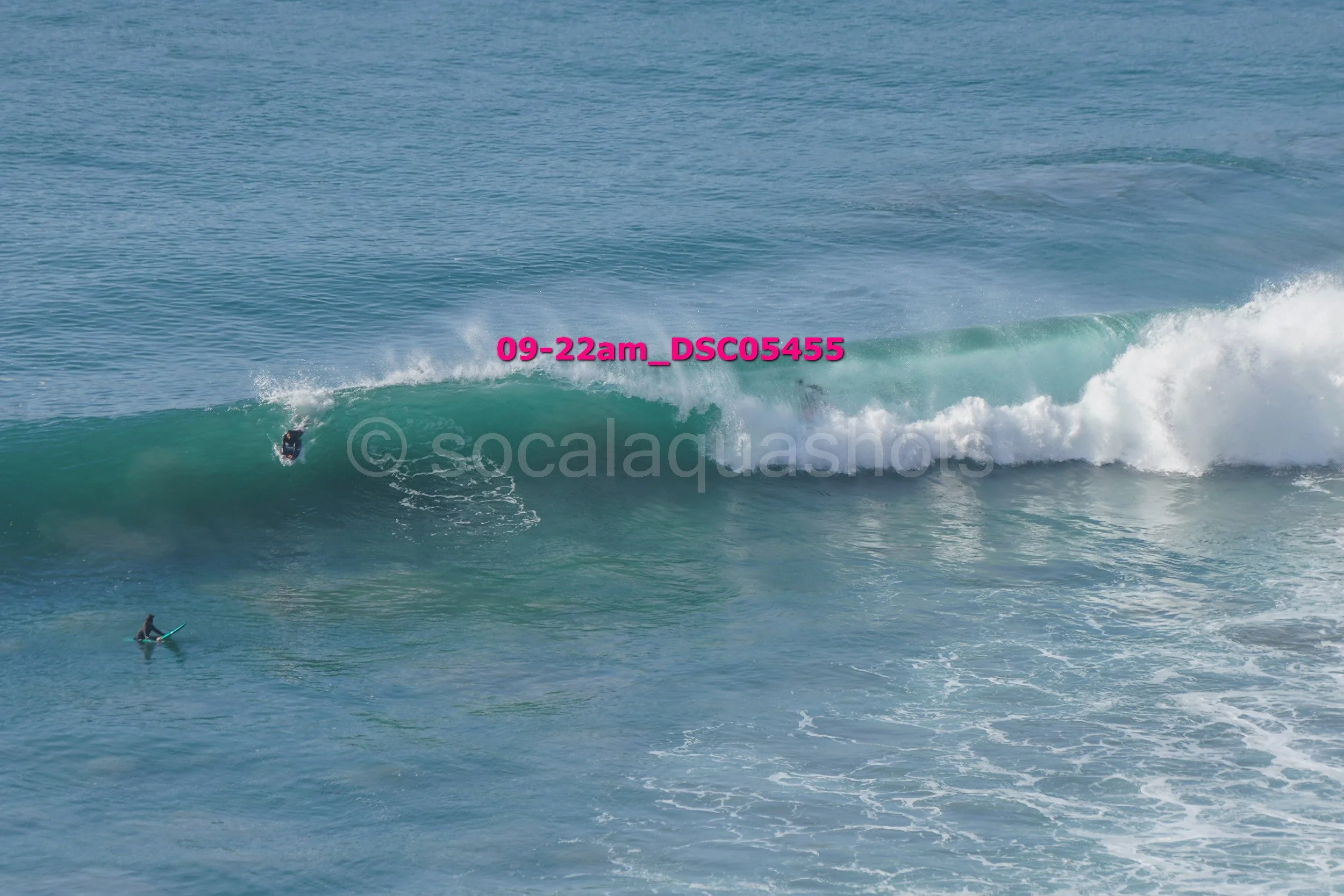 A surfer riding a wave in the ocean with another person paddleboarding nearby.