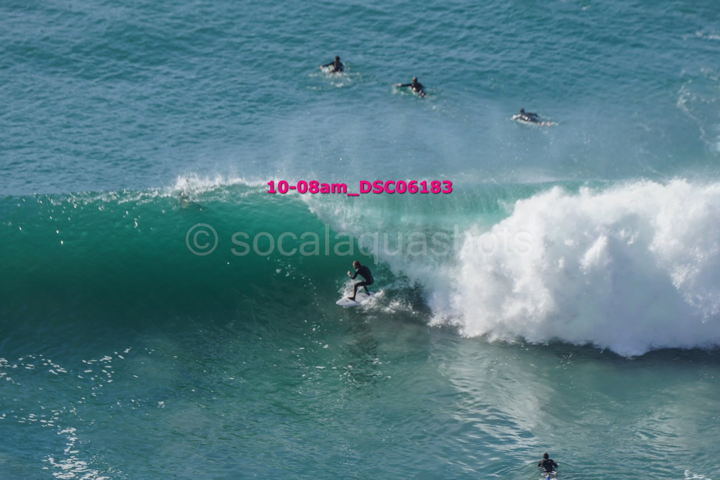 Surfer riding a large wave with three other surfers in the background, in the ocean.